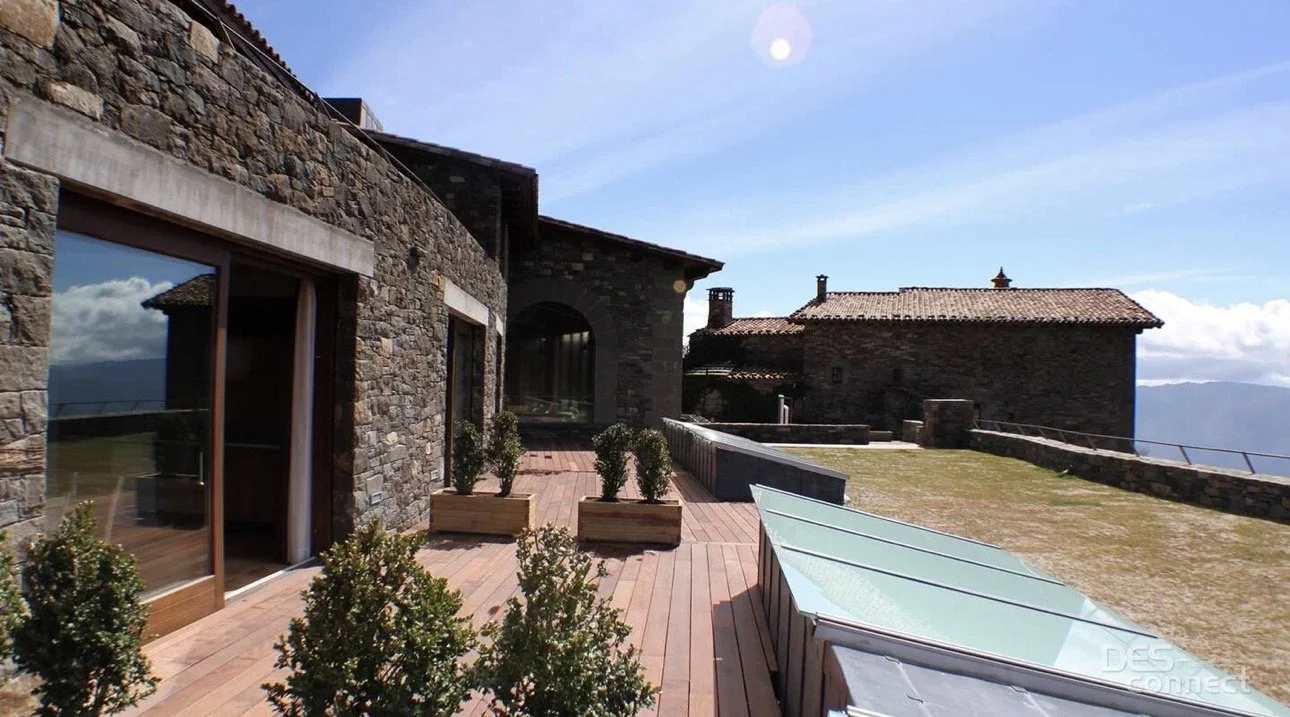 Terraza en una casa de piedra en las montañas con plantas en macetas, ventanas grandes y una vista del cielo y las montañas
