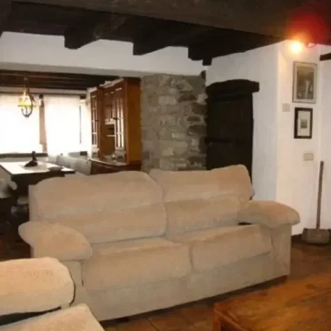 Sala de estar con sofá beige, paredes de piedra y techo con vigas de madera.