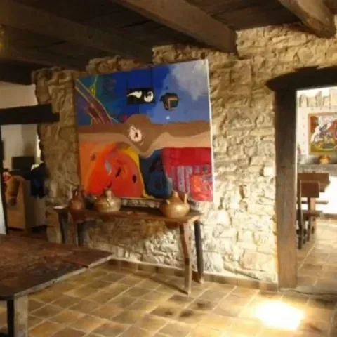 Una pintura abstracta en una pared de piedra en un interior con mobiliario de madera.