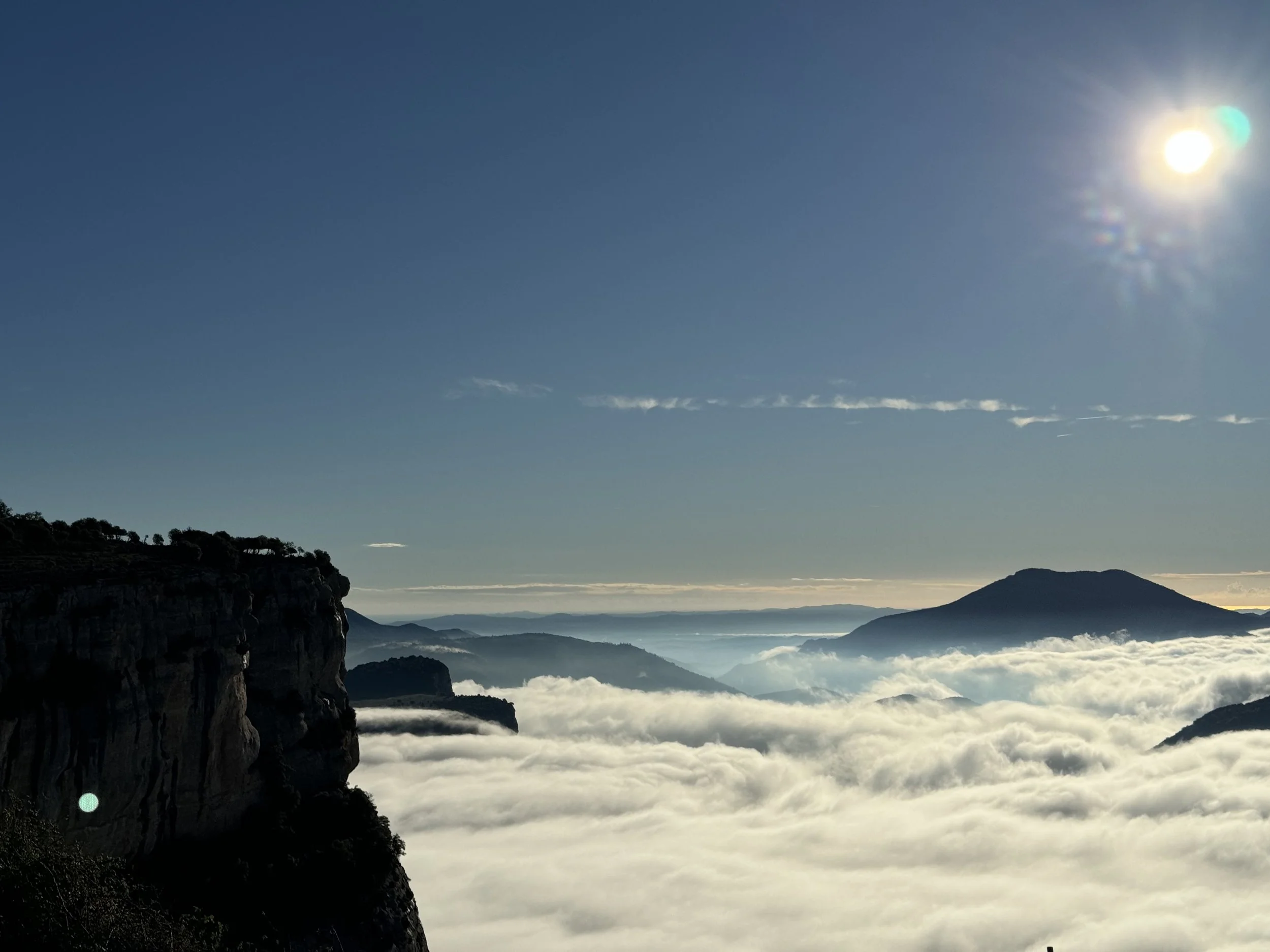 Paisaje de montañas con nubes y cielo despejado con sol brillante.