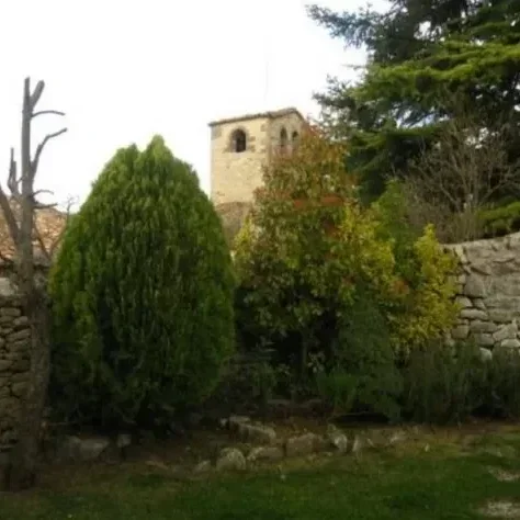 Jardín con arbustos y árboles, en el fondo una torre antigua de piedra y muro de piedra.