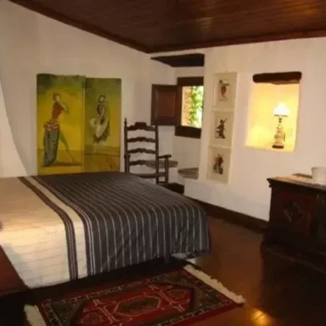 Habitación con cama, cuadros en la pared, ventana con vista a los árboles, y mueble de madera.