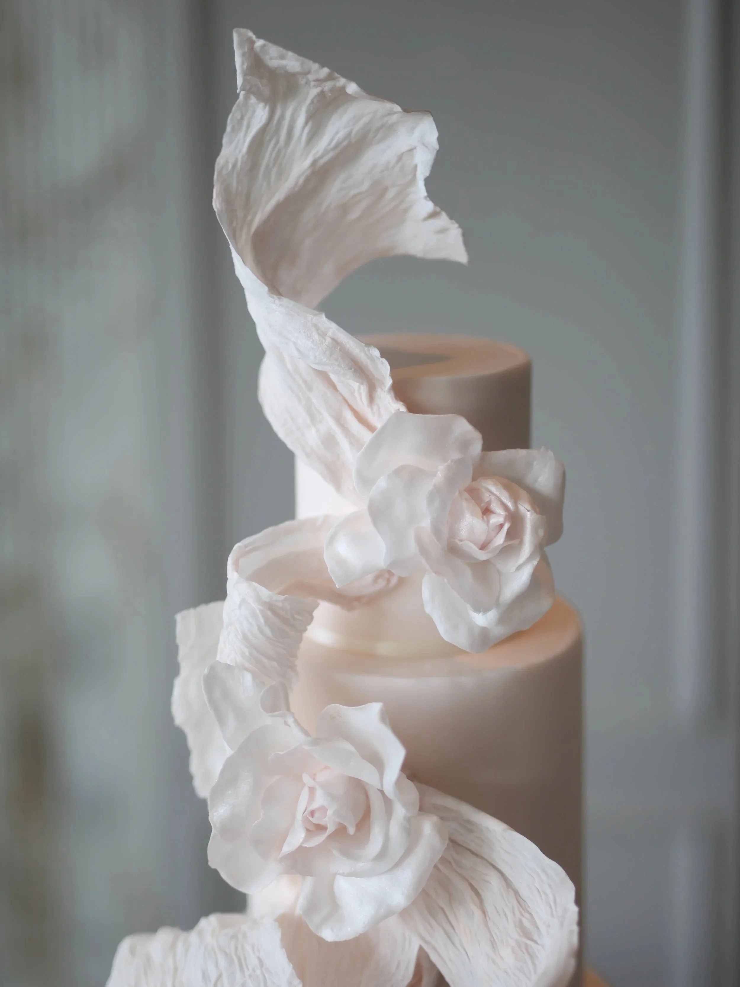 Close-up of a contemporary cake with delicate pink sugar flowers and flowing sculptural edible details.