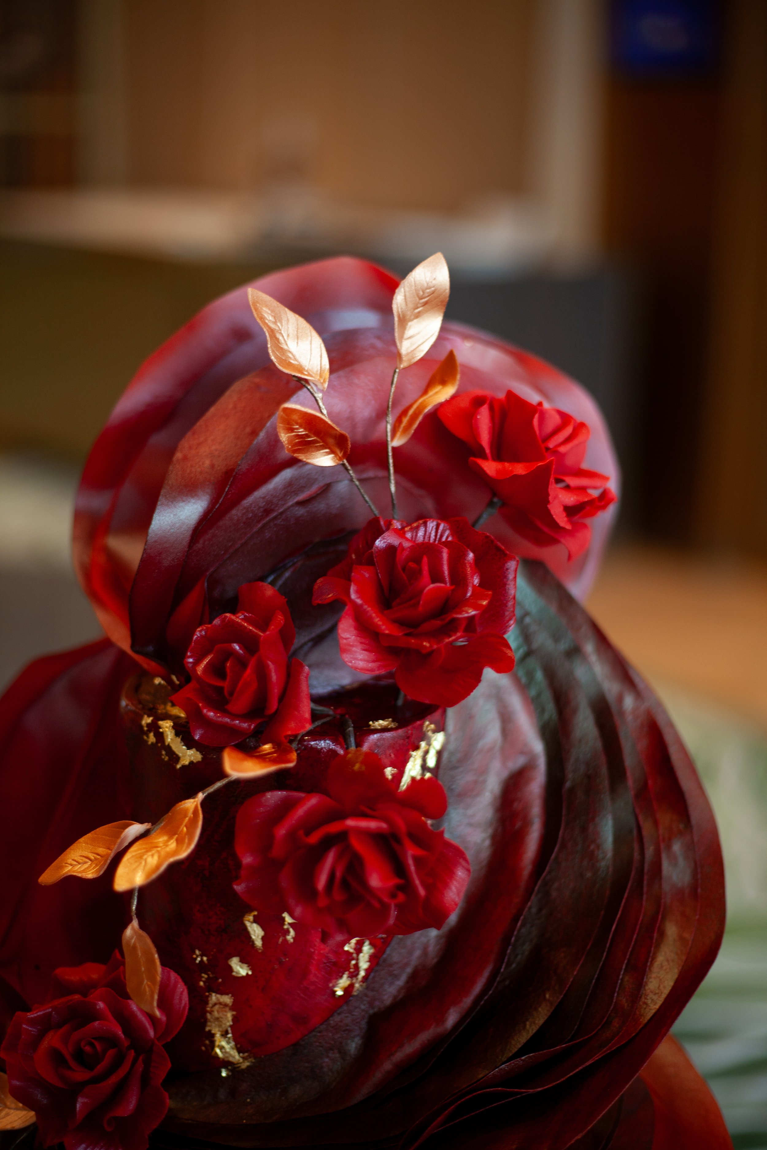 Close-up of a sculptural cake with handcrafted red sugar flowers and gold botanical details.