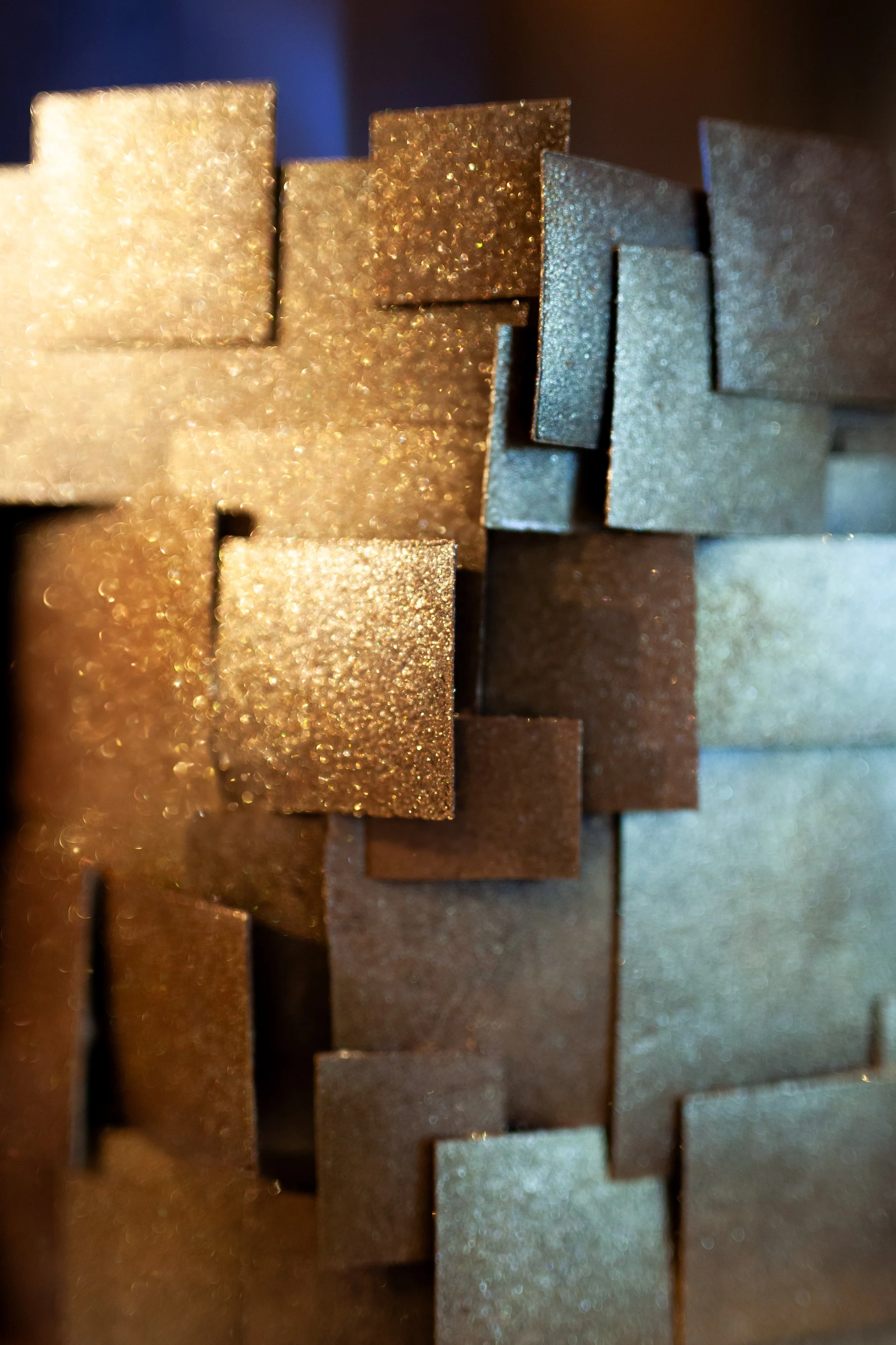 Close-up of various metallic metallic blocks with textured or glittery surfaces, arranged in a staggered pattern.