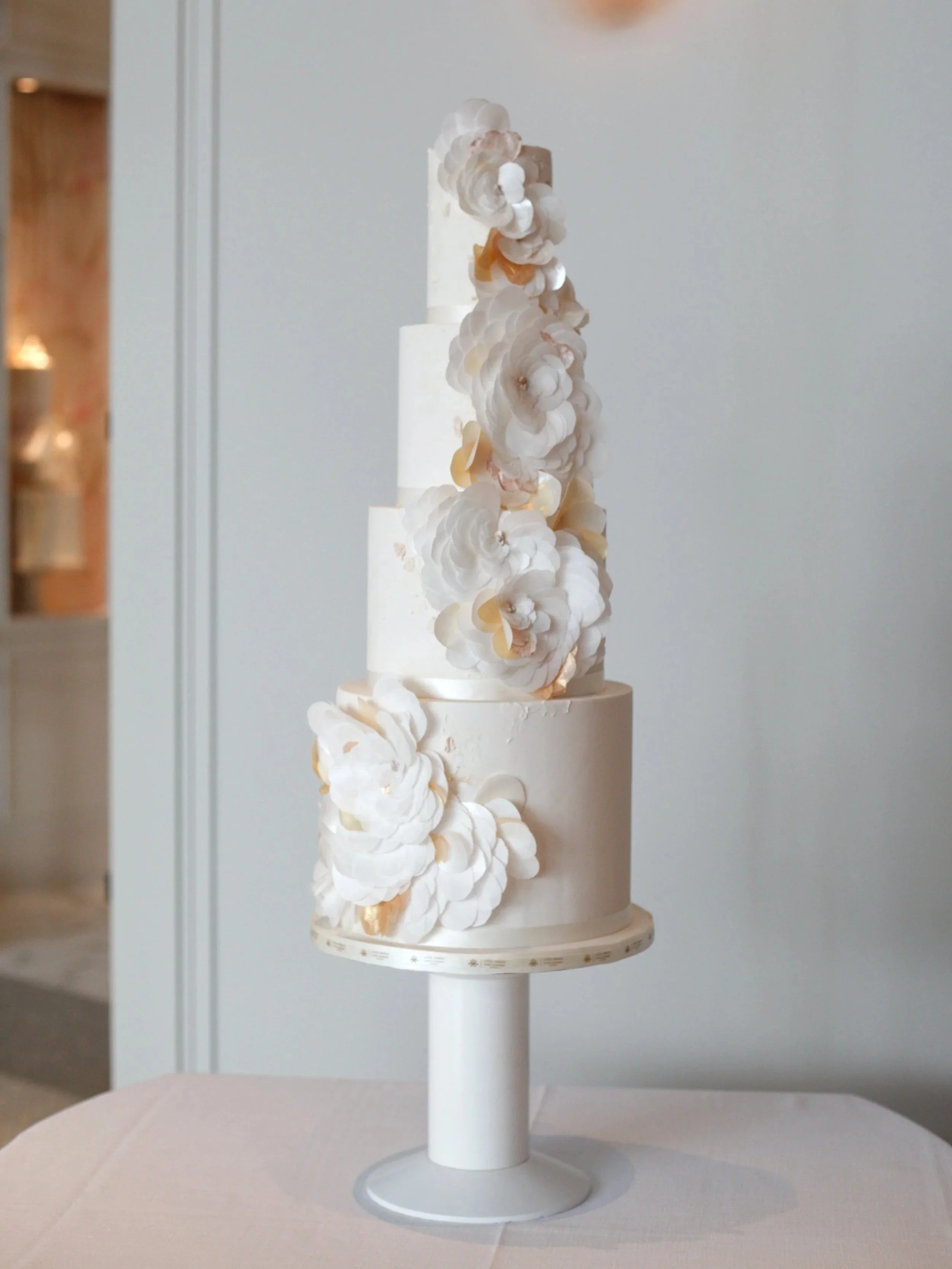 Elegant three-tier white wedding cake with delicate ivory sugar flowers and sculptural botanical details.