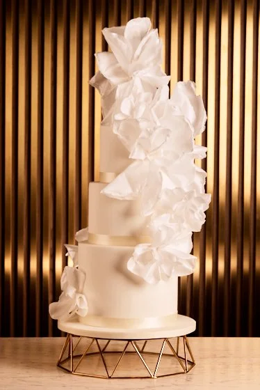 Contemporary white wedding cake with large sculptural sugar flowers and flowing edible details.