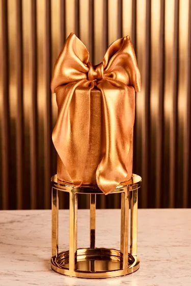 Sculptural gold gift box cake wrapped with an oversized satin-effect bow.