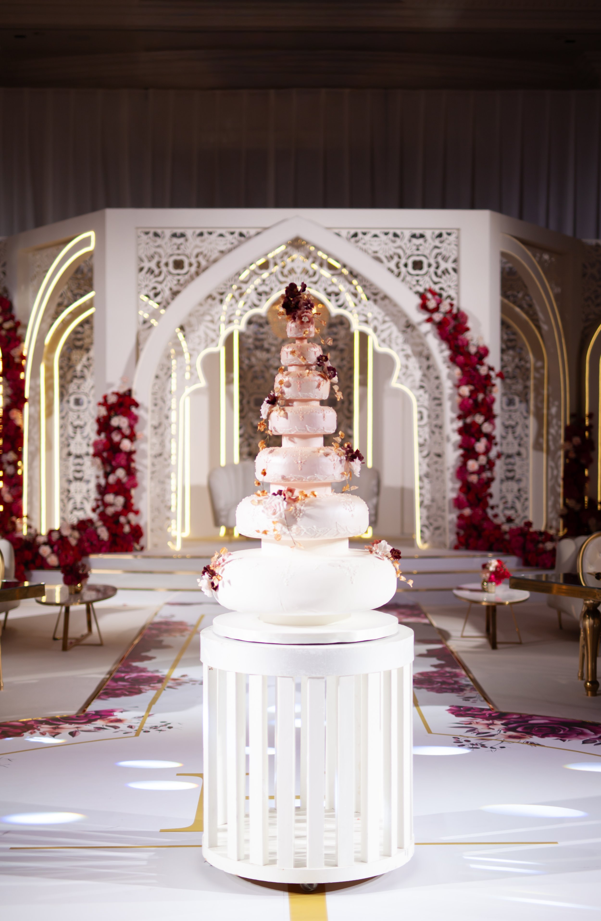 Multi-tier wedding cake with delicate floral details displayed in an elaborate luxury wedding setting.