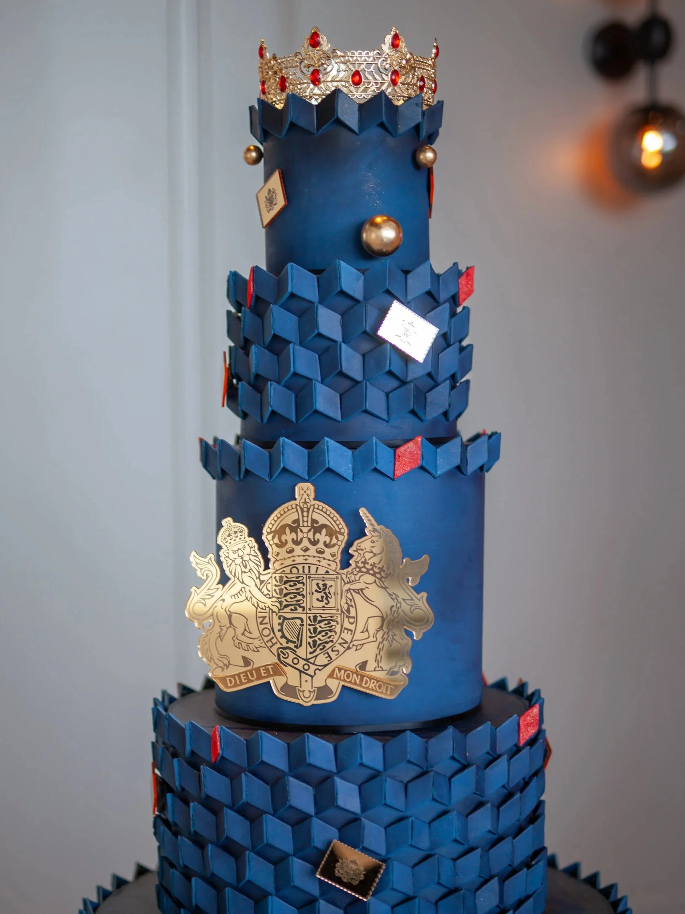 Bespoke blue celebration cake with geometric detailing, Royal Crest, ornate gold elements and a sculptural crown for HRH King Charles 3 and The British Embassy.