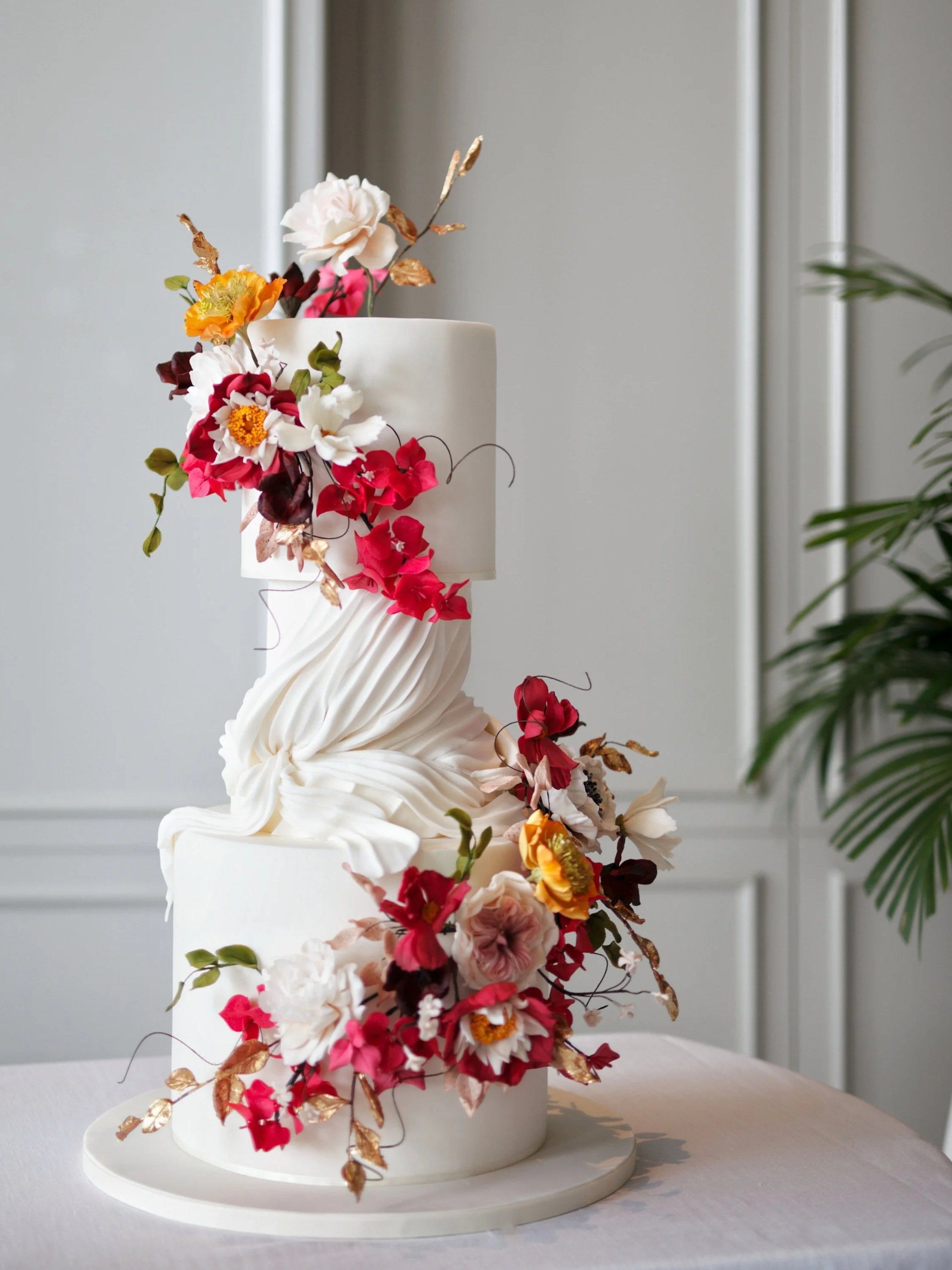 Tall white wedding cake with cascading colourful sugar flowers, foliage and delicate gold details.