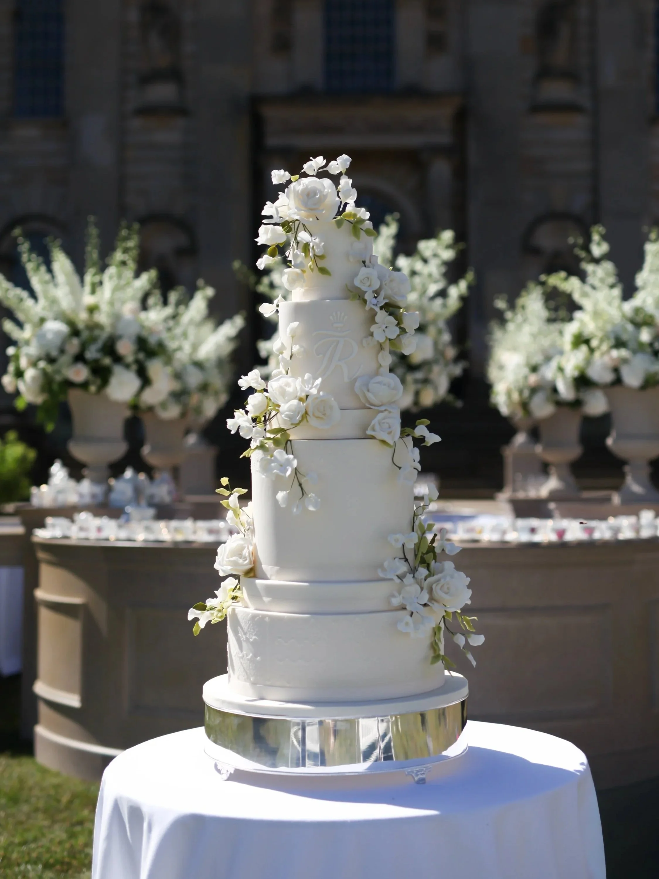 Tall multi-tier wedding cake with white sugar roses and delicate botanical details in an elegant outdoor setting of Howard Castle.