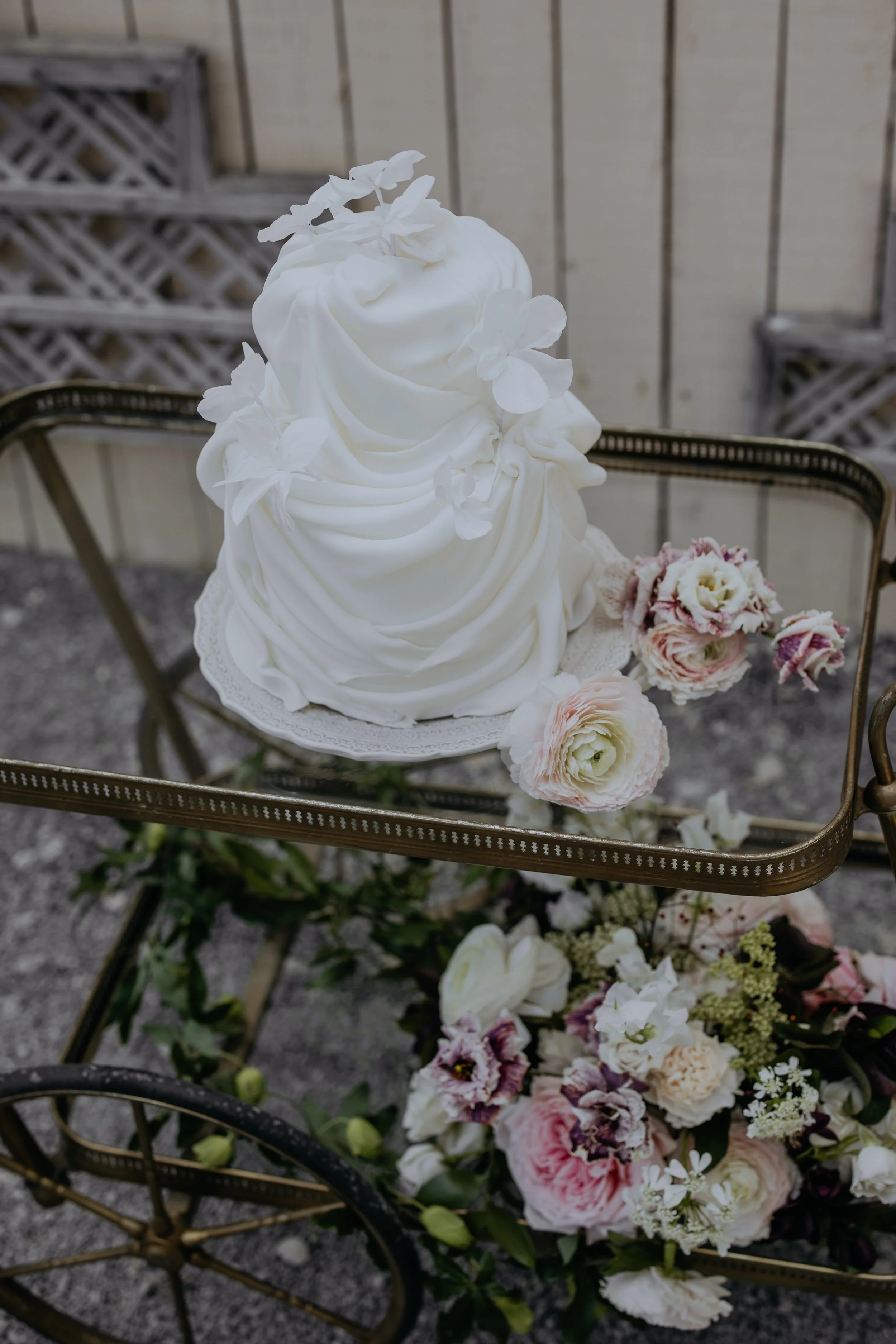 Elegant white wedding cake with delicate sugar flowers and butterflies, displayed on a vintage cake stand.