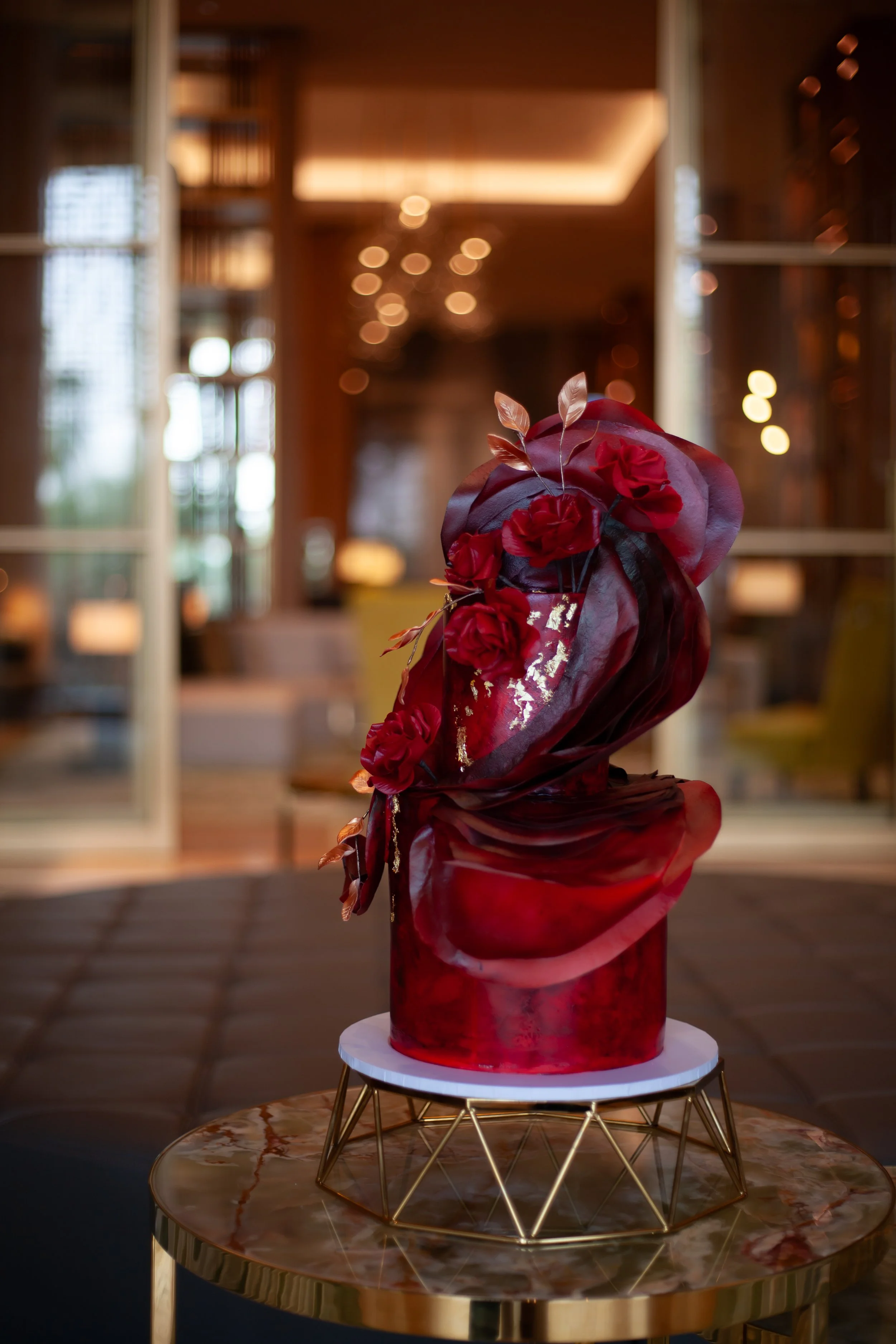 Sculptural red cake decorated with dramatic red sugar roses and gold leaves.