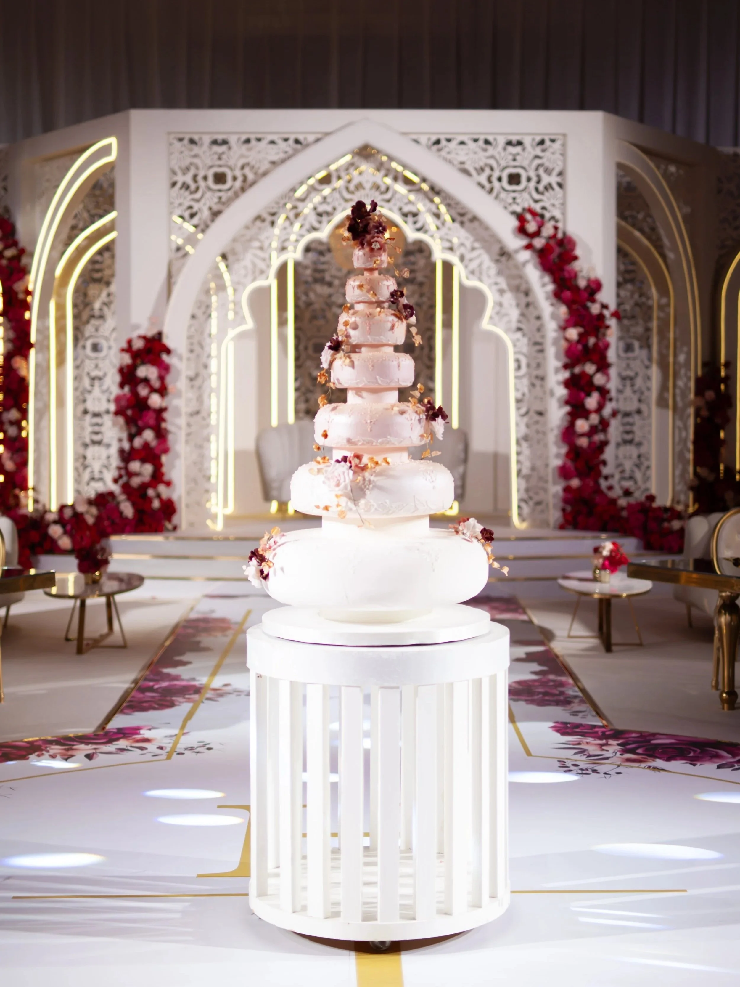 Multi-tier wedding cake with delicate floral details displayed in an elaborate luxury wedding setting.