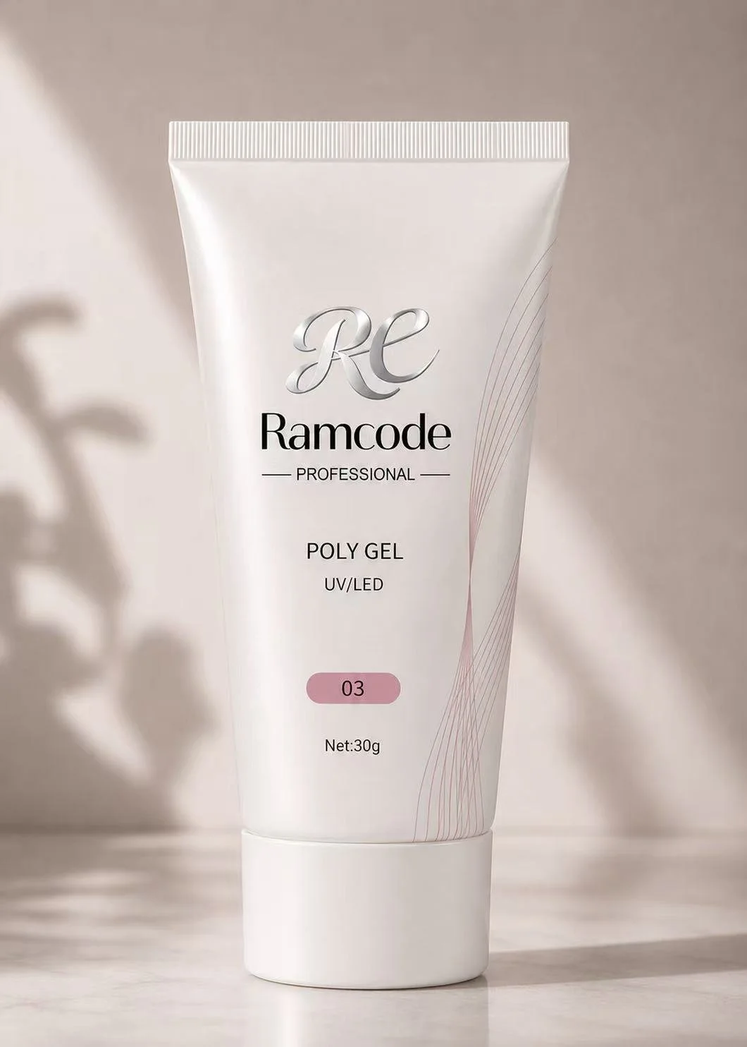 A white tube of Ramcode professional poly gel UV/LED nail product standing on a flat surface with a beige background with a shadow and blurred plant shadow in the background.