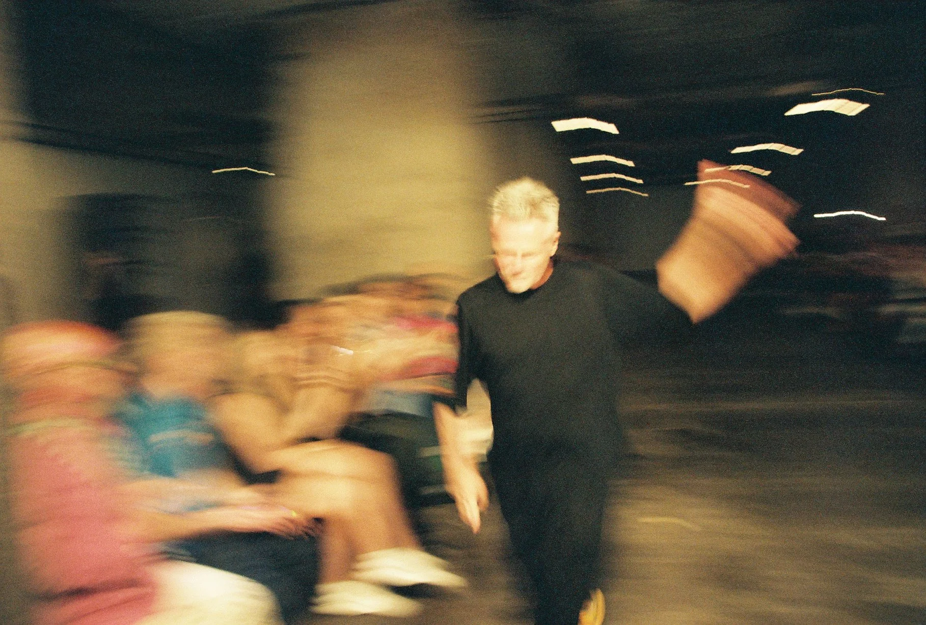 A person with blonde hair in a black shirt walking through a blurred crowd at night, with lights and people in the background.