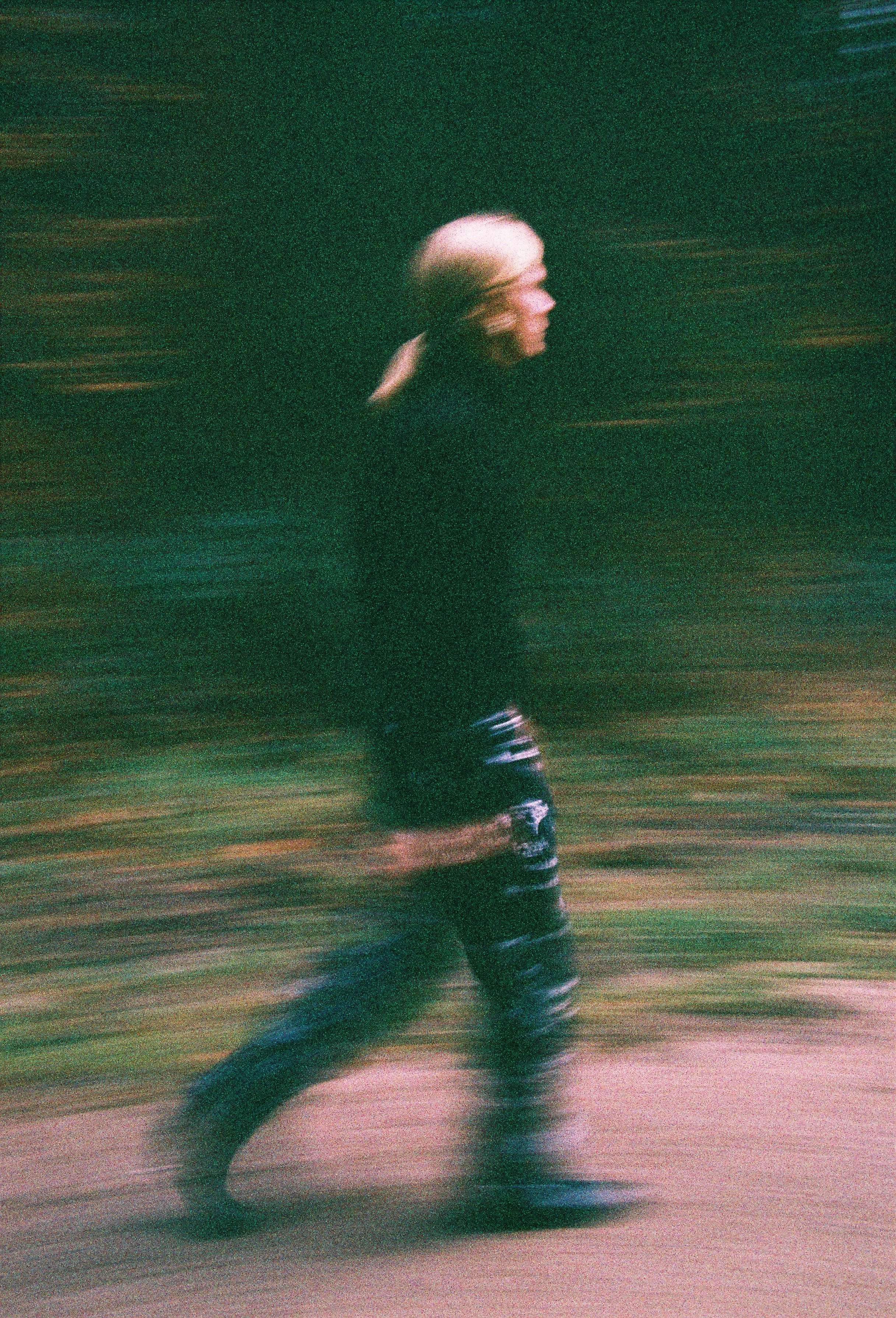 A person running on a track during the night, wearing dark clothing and athletic shoes, captured with motion blur.
