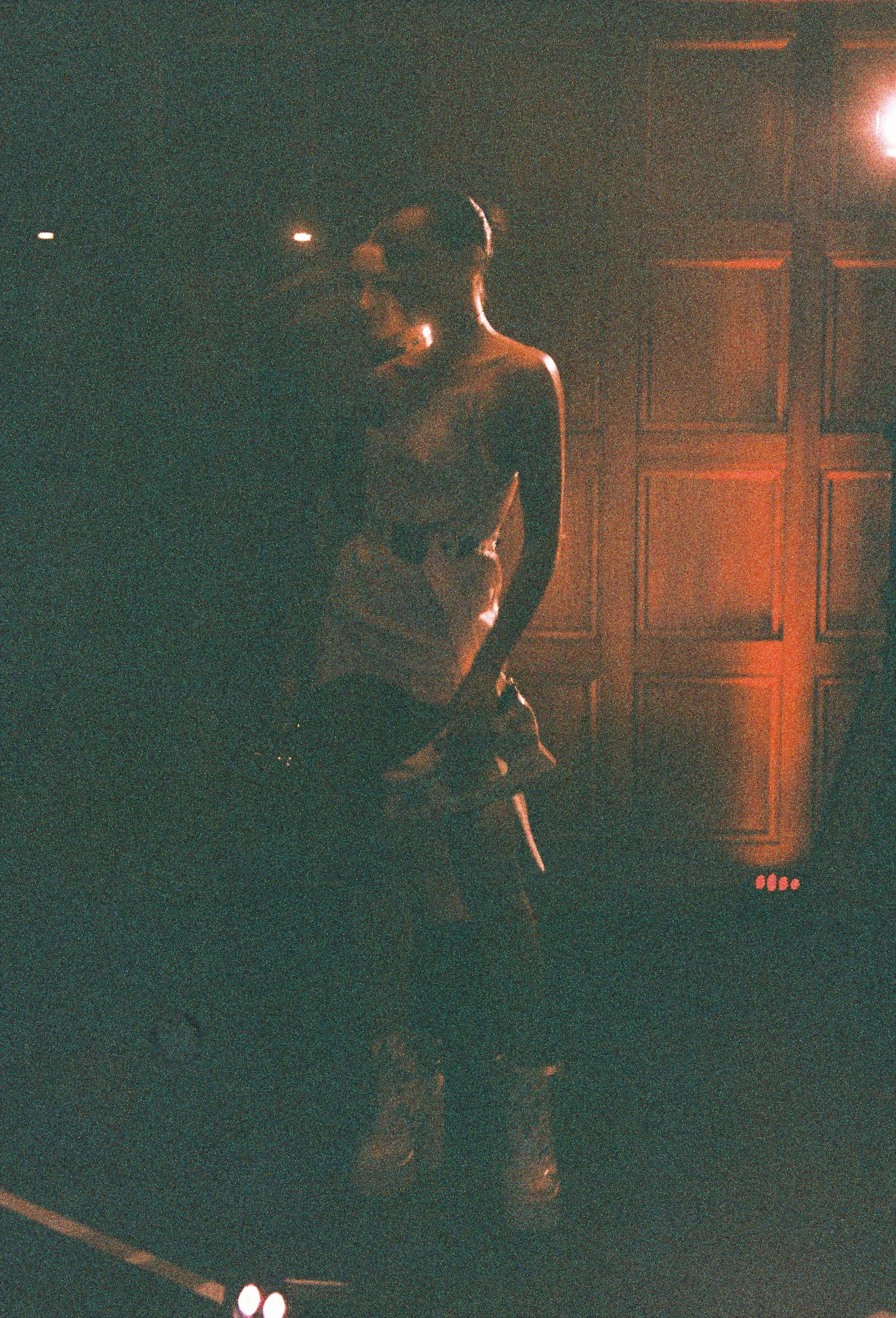 A person standing in a dimly lit room with orange lighting, a wooden panel wall, and some electronic equipment with lights.