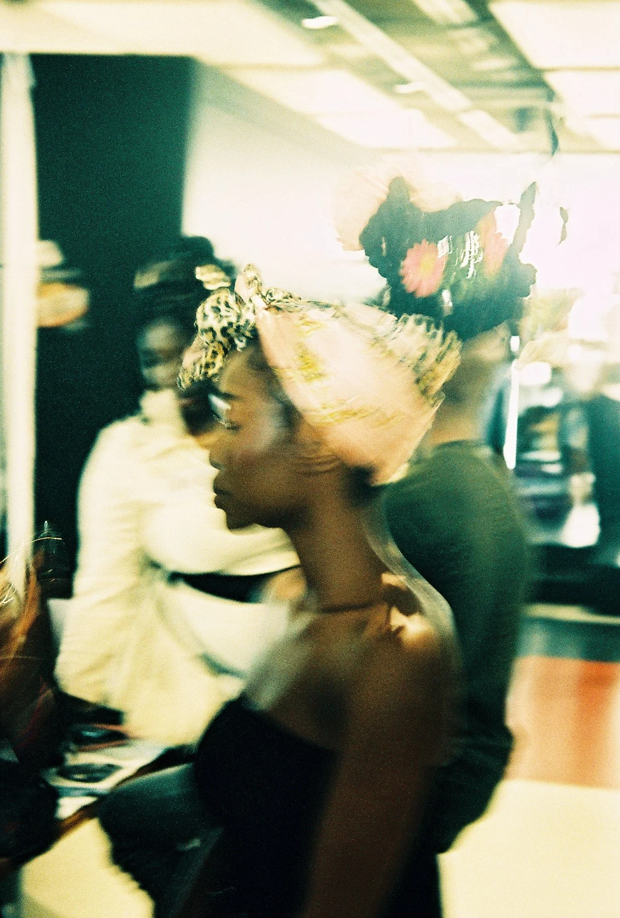 A woman wearing a colorful headscarf is seated, surrounded by other people in what appears to be an indoor setting, possibly a restaurant or café. The image is blurry and overexposed.