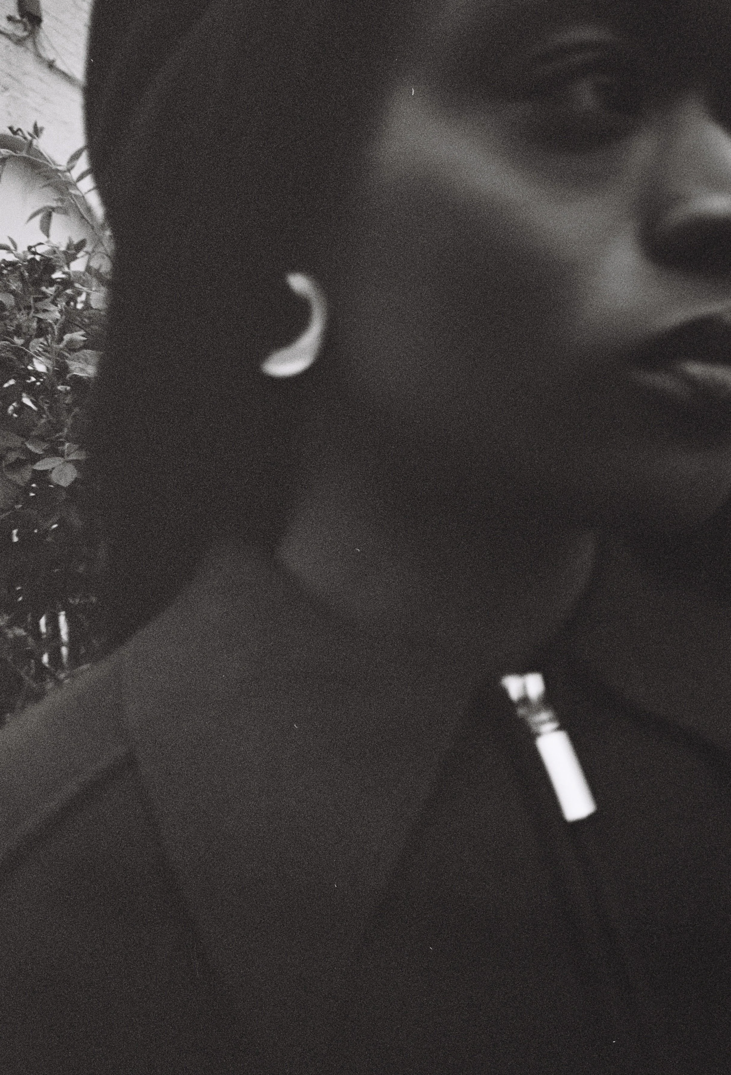 Close-up of a person's face, partially in shadow, with a lollipop in their mouth and a background that includes trees and a wall.