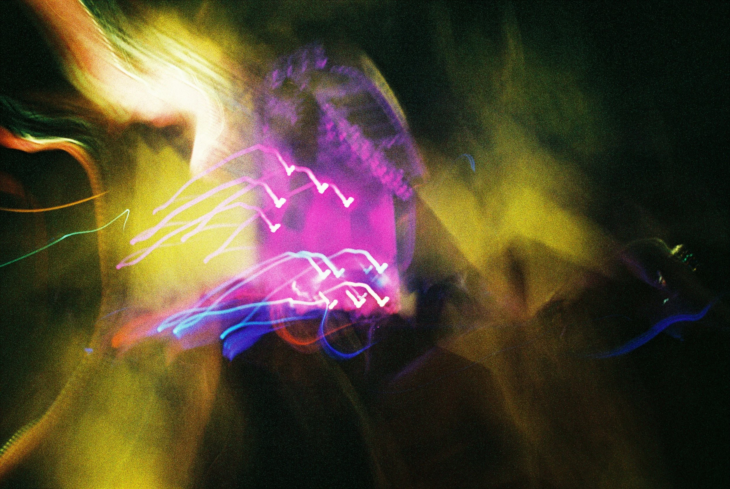 A long exposure photograph of multicolored light trails creating abstract patterns against a dark background.