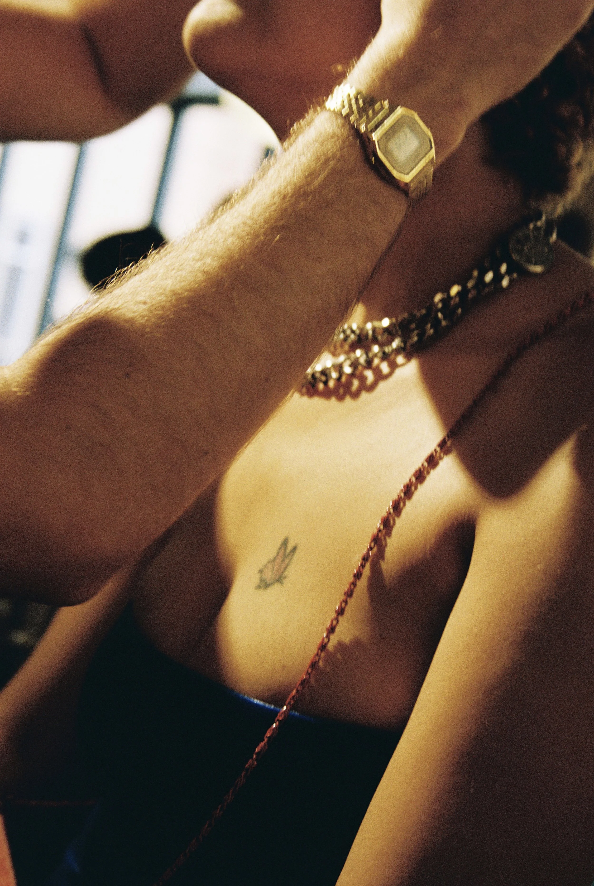 Close-up of a person's wrist with a gold watch and jewelry, and part of their shoulder and chest visible, featuring a small tattoo of a butterfly.