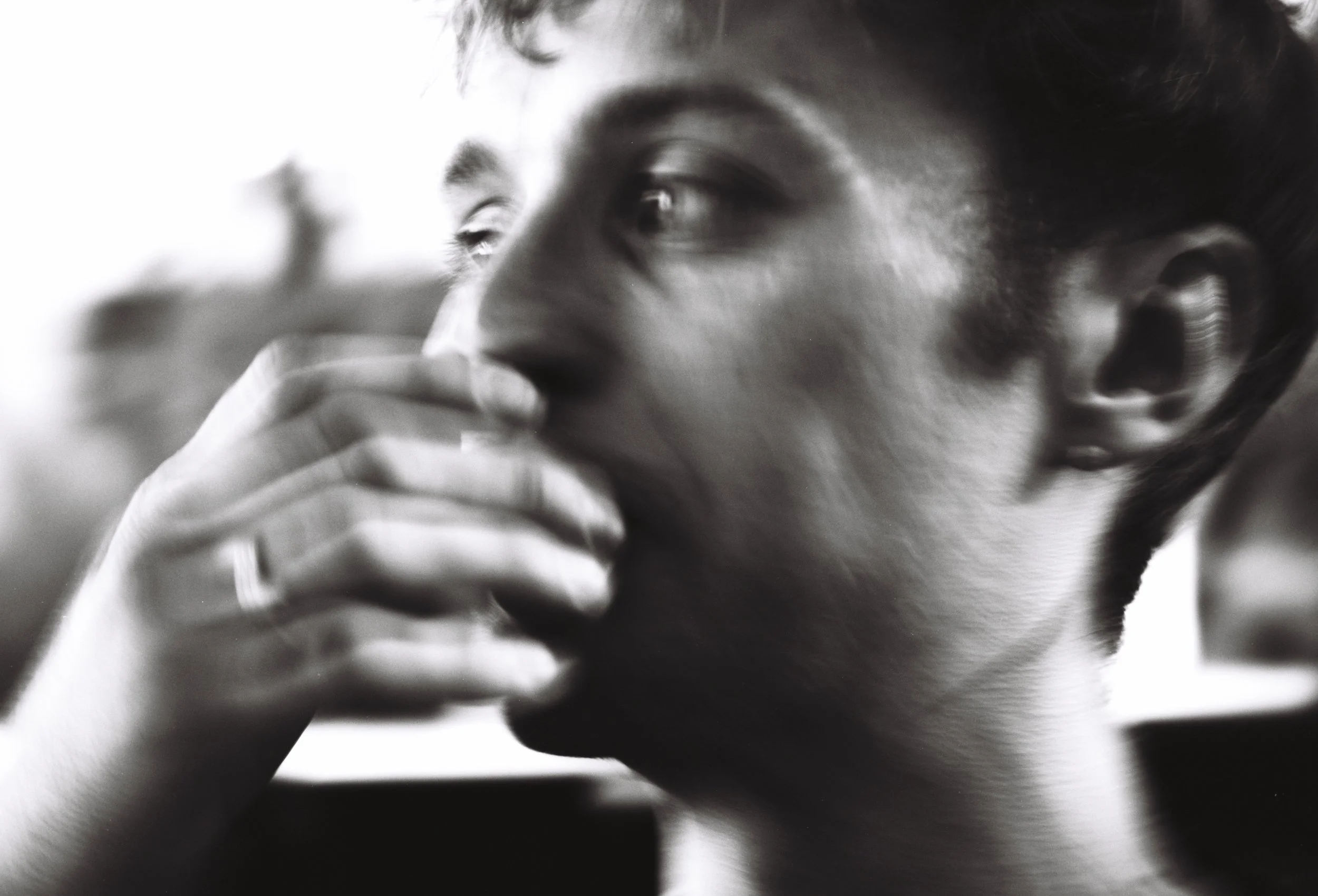 Close-up black and white image of a person's face, focusing on their eye and hand touching their lips.
