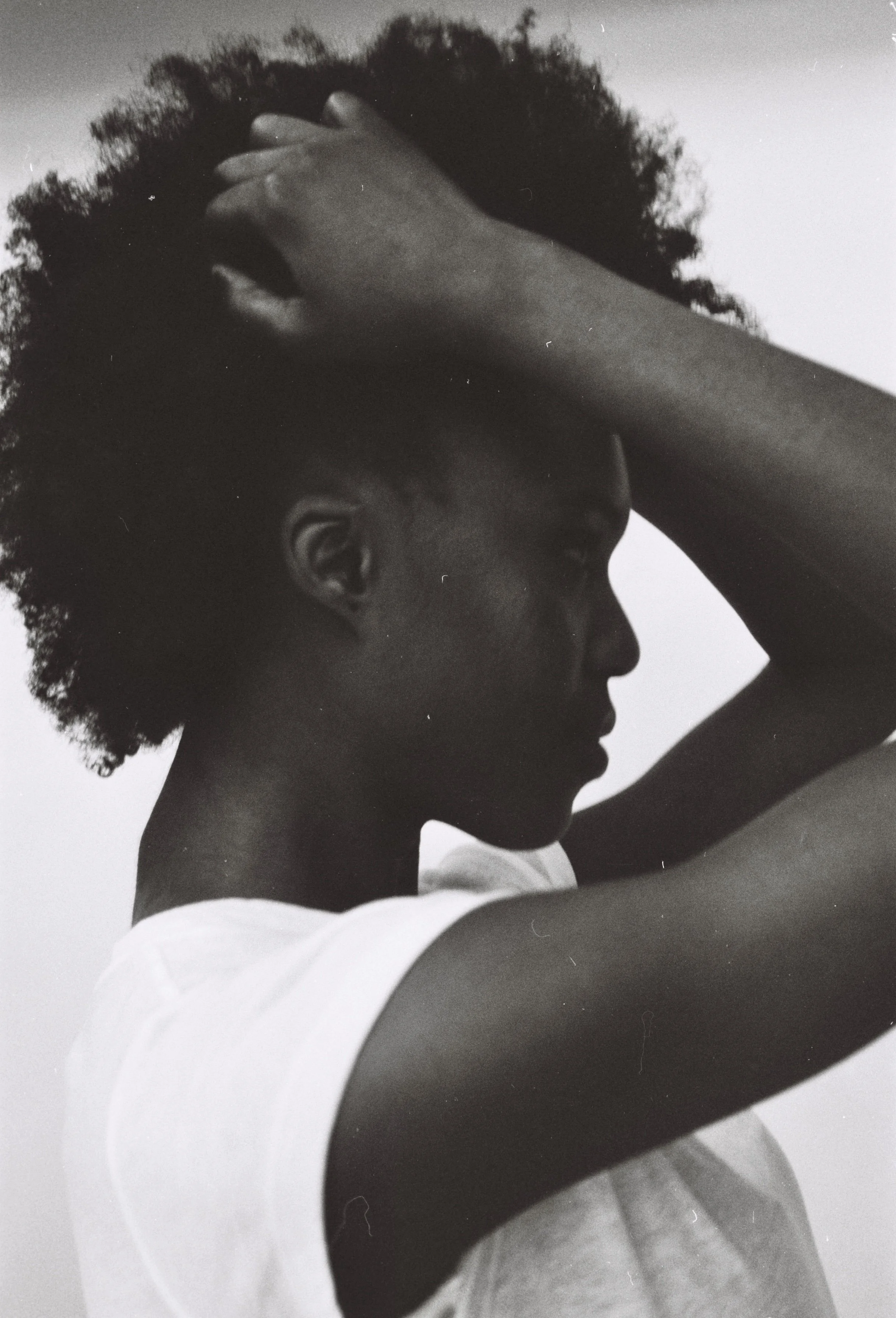 A black and white side profile of a woman with natural curly hair, looking down with her hand resting on her head.