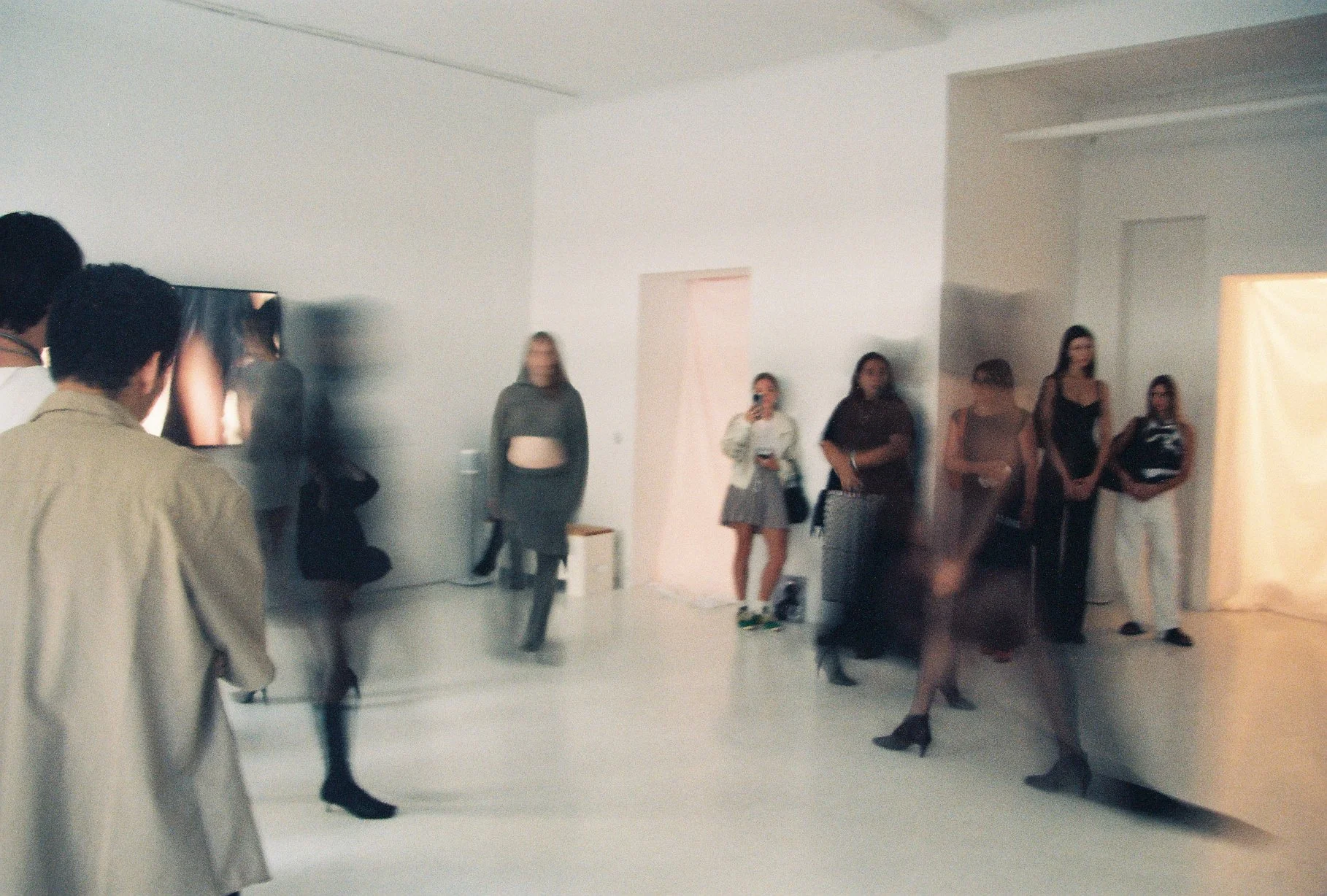 A group of people standing and walking in an art gallery or exhibition space with plain white walls and a minimalistic interior.