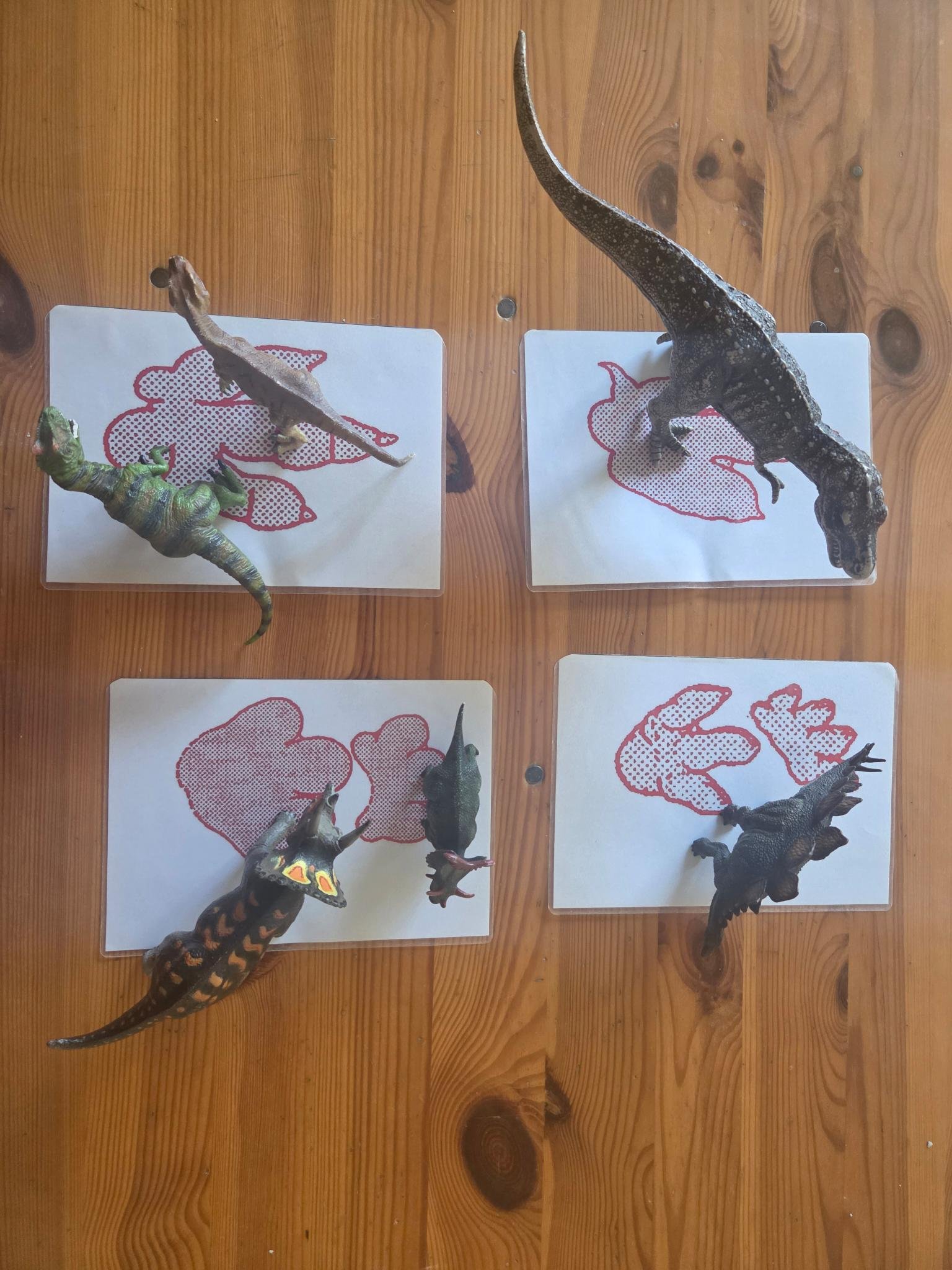 Modèles réduits de dinosaures posés sur des images d'empreintes de pas, sur une surface en bois.