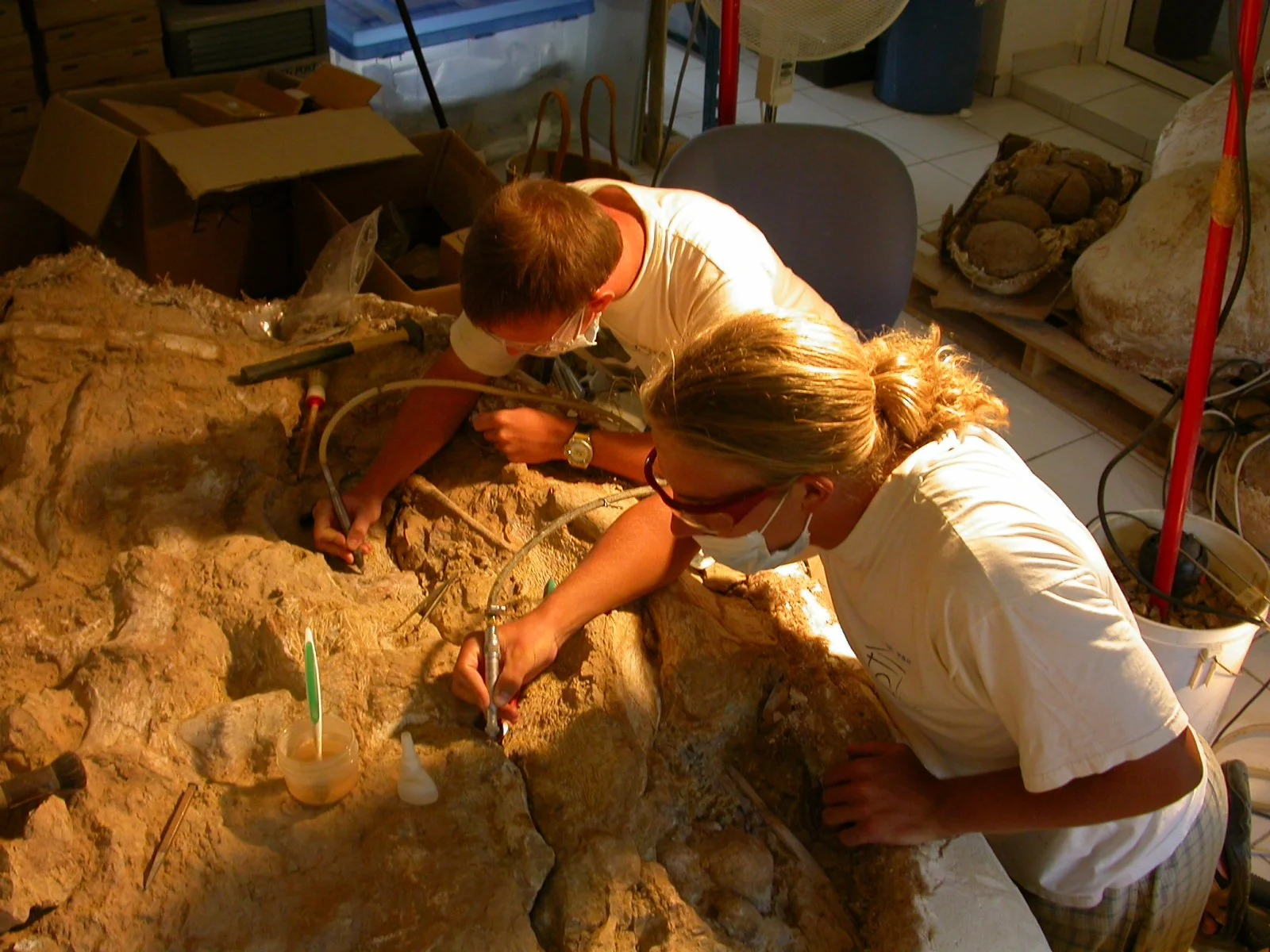 Deux archéologues ou chercheurs examinent et restaurent une ancienne structure en pierre dans un laboratoire.