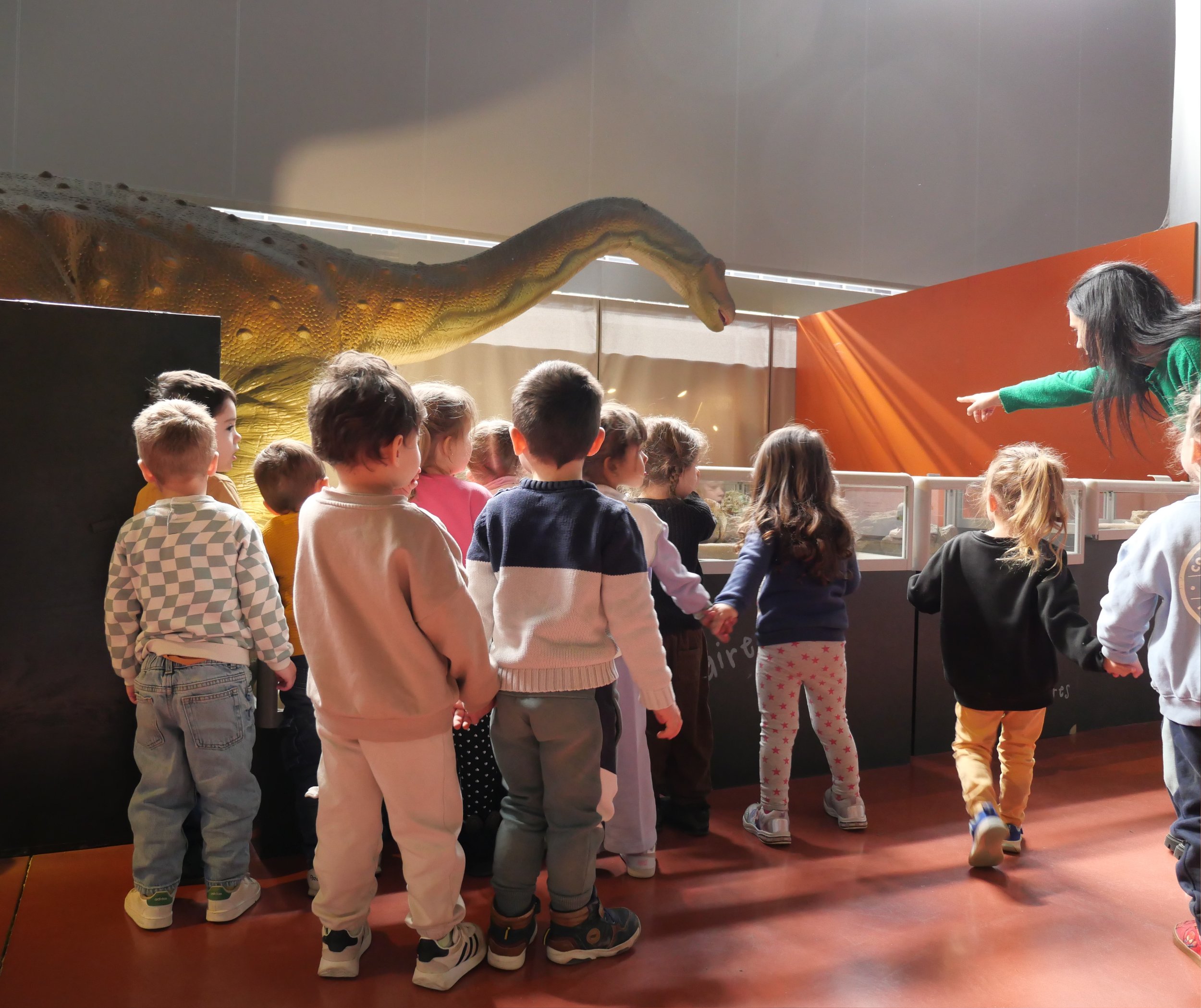 Un groupe d'enfants regardant une exposition d'animaux, dont un énorme python enroulé au plafond.