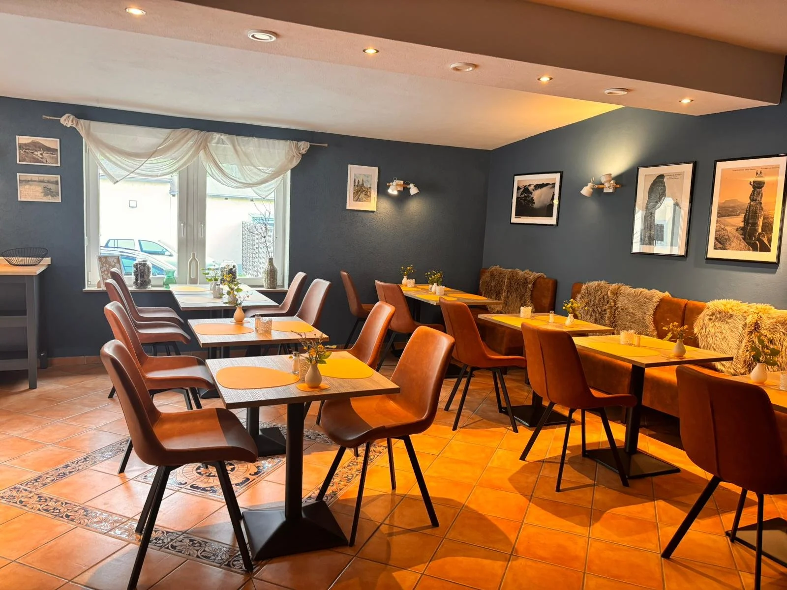 Ein gemütliches Restaurantsinterieur mit mehreren Tischen, braunen Stühlen und Wandbildern an einer blauen Wand.