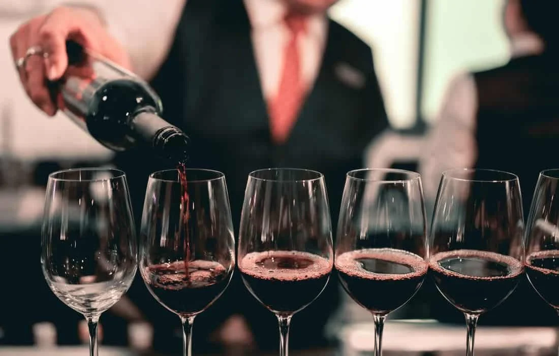 Smartly dressed man pouring red wine into a number of wine glasses for a wine tasting.