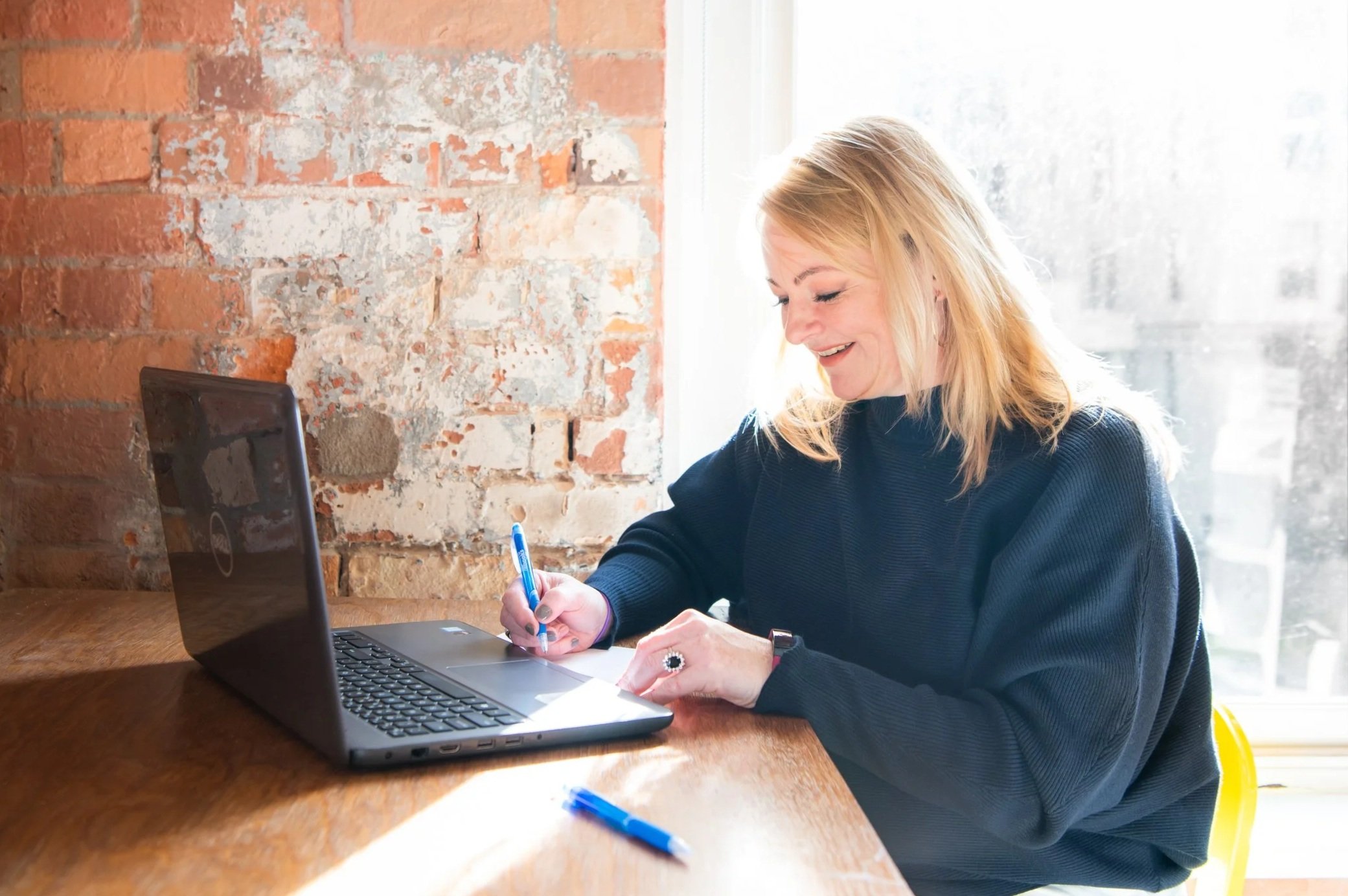 your accountant raquel dukic sitting at a desk by a brighlty lit window wth a black laptop in front of her holding a blue pen.