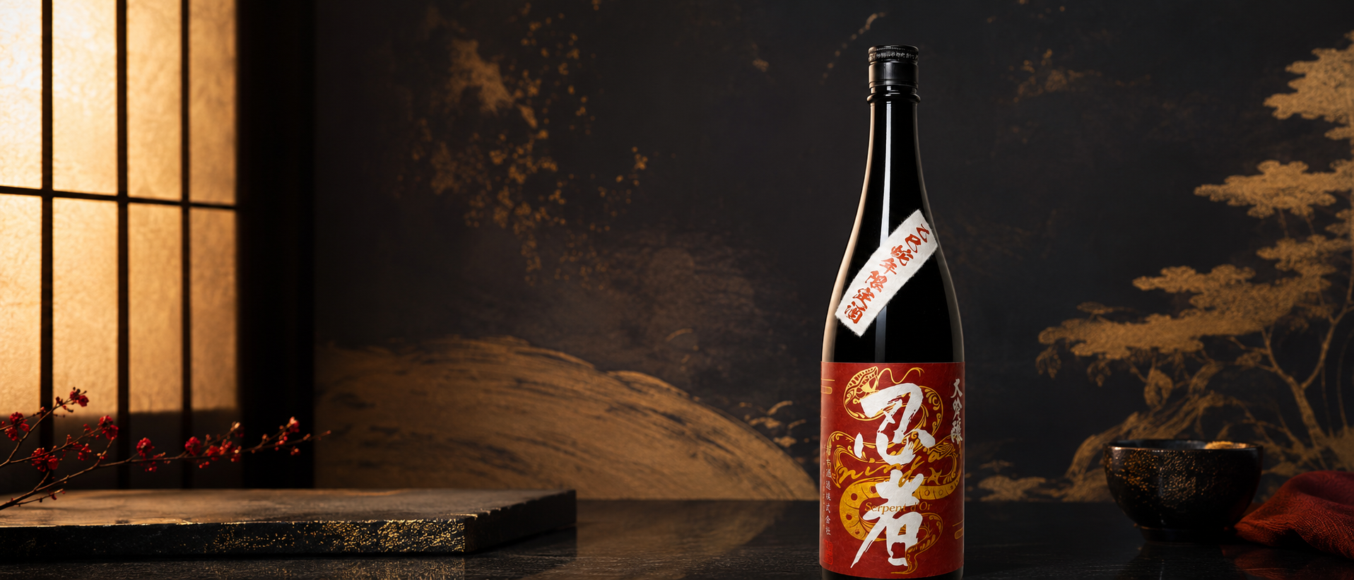 A black bottle of Ninja Kinnohebi Daiginjo with red and gold Dragon design, with Japanese and English labels, positioned on a dark table in front of a traditional Japanese-style paper screen with warm lighting, a small bowl, and a red cloth.