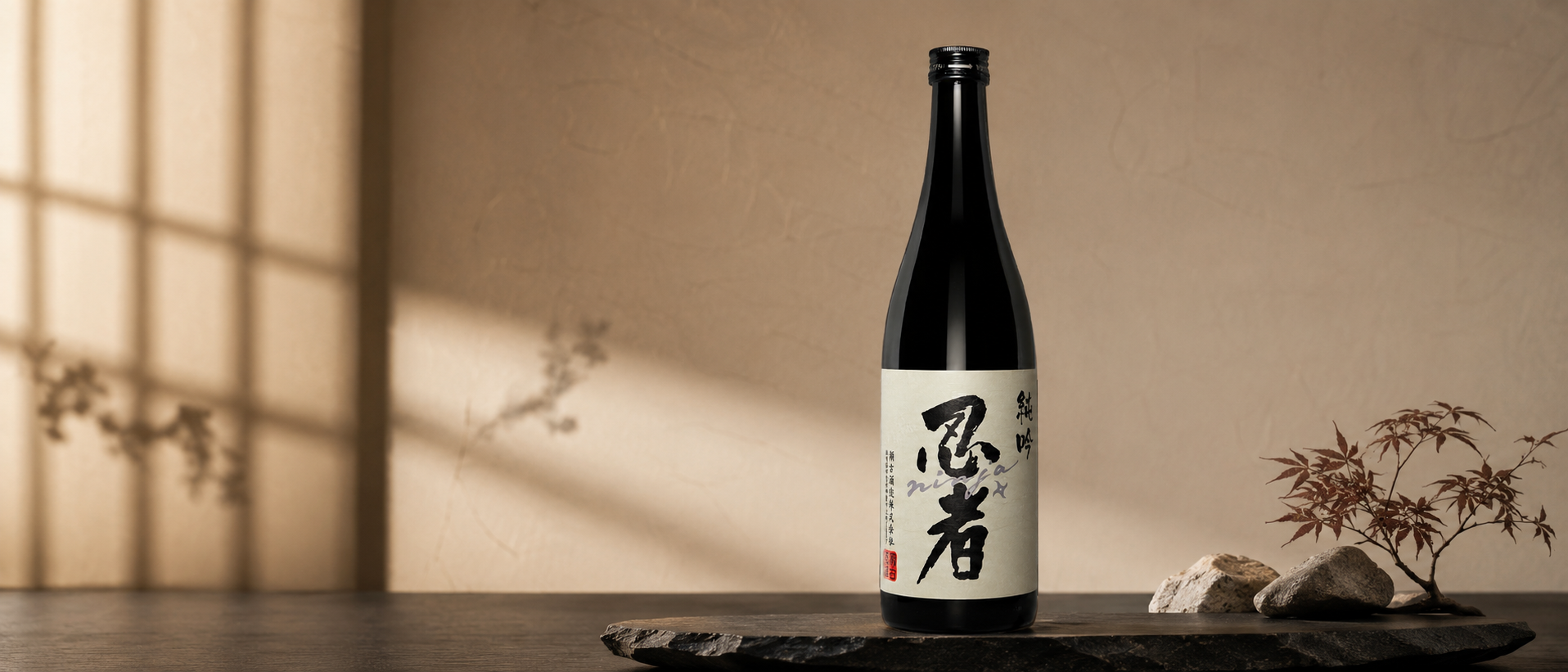 A bottle of Ninja Shiro Junmai Ginjo on a black wooden tray with rocks and a small potted Japanese maple tree, against a beige wall, with soft lighting and shadows.