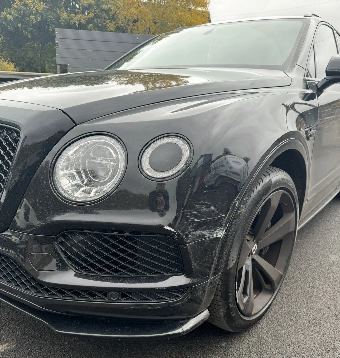 Black luxury SUV with damage on front right bumper below the headlight, parked outdoors.