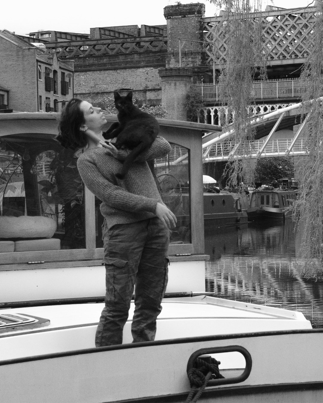 Black and white image of a woman on a barge being climbed on by a cat 