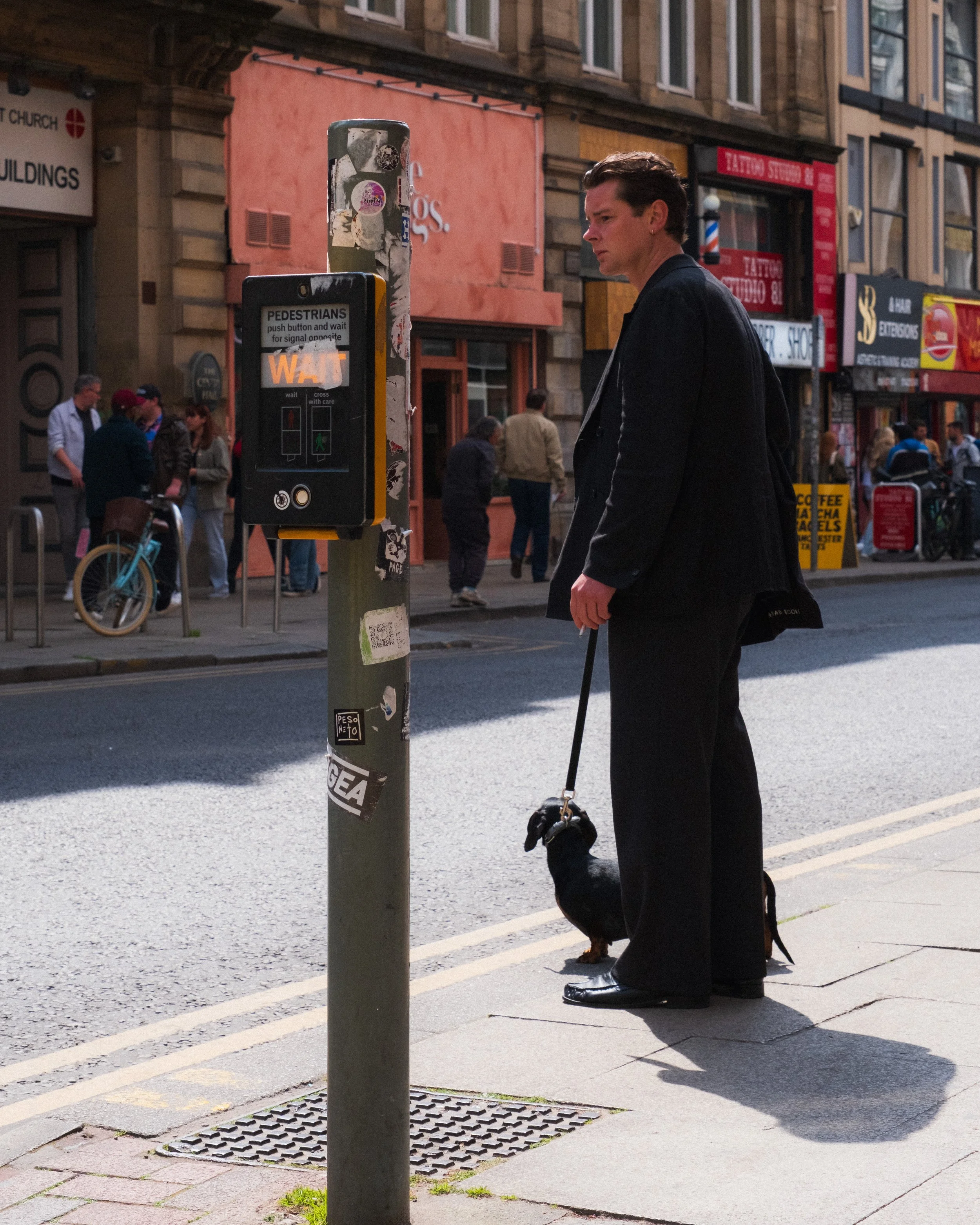 Suited man smokes a cigarette waiting to cross the street with his dog 