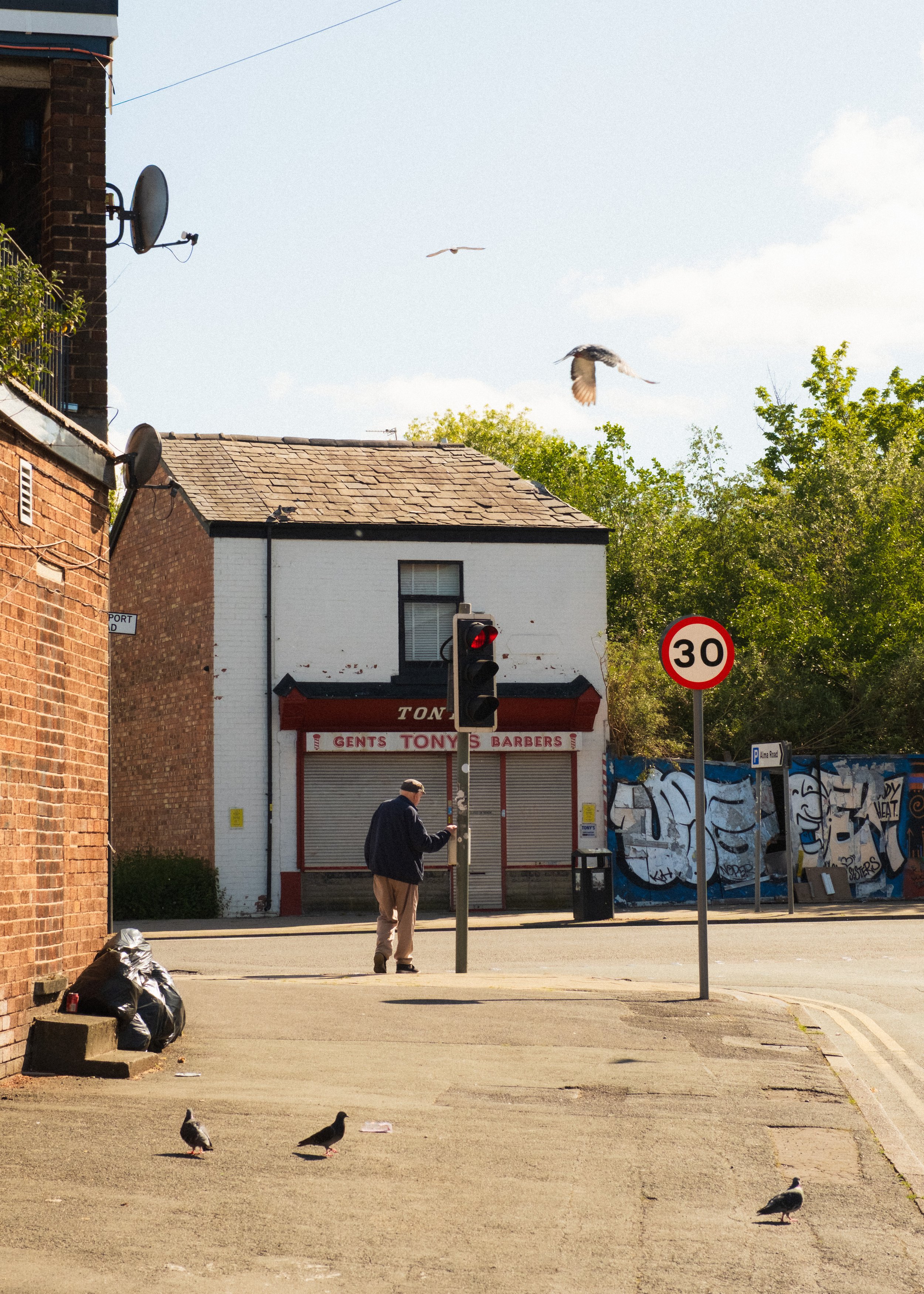 Man crosses the road in Levenshulme with pigeons alongside him