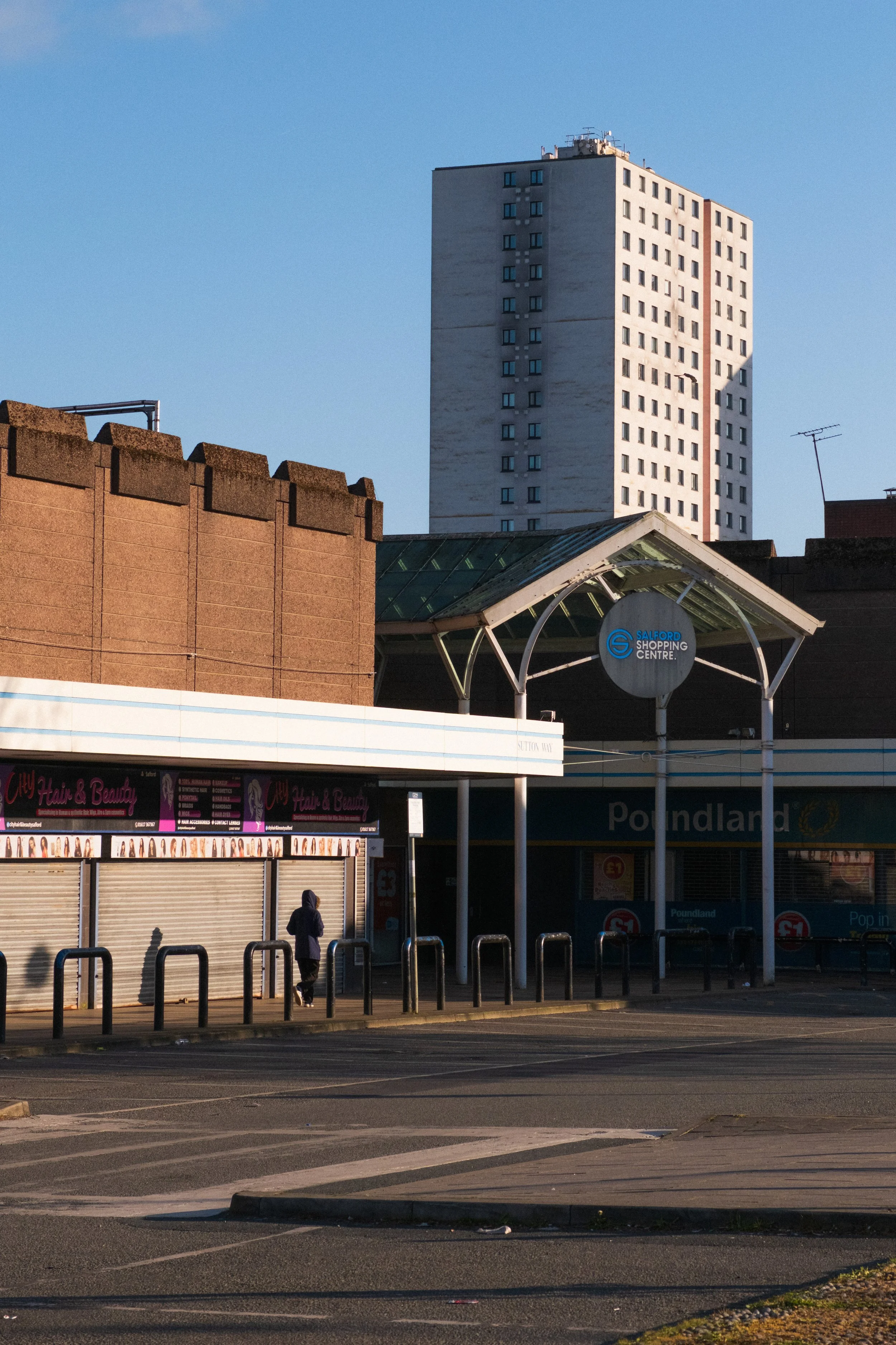 Hooded man walks towards shadows in Salford precinct