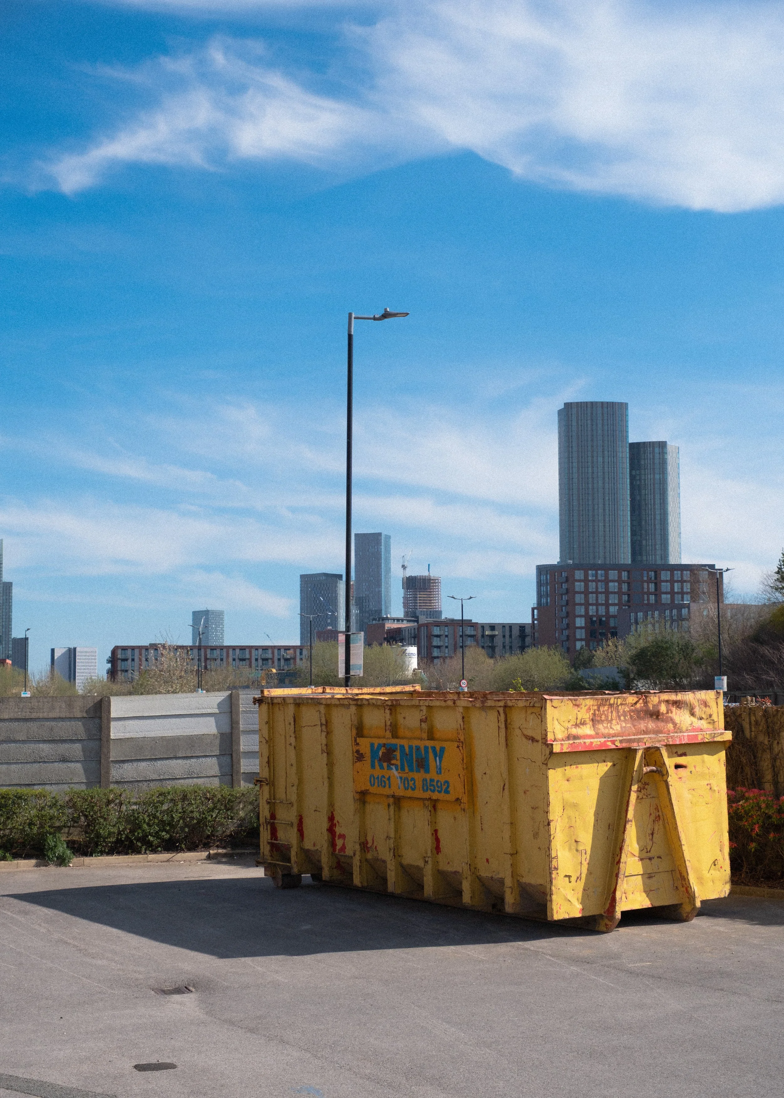 Yellow skip against blue background and manchester skyline