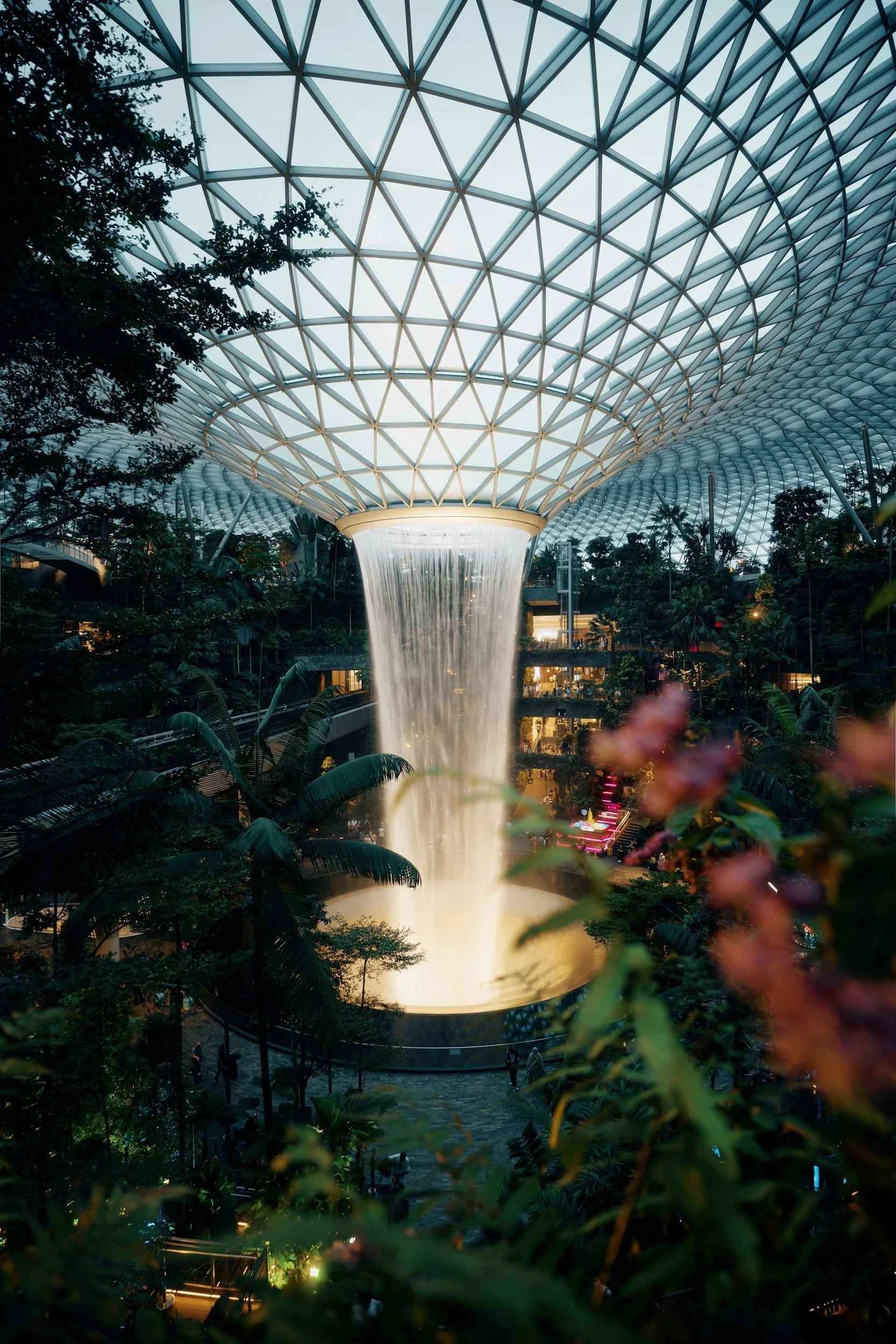 Indoor indoor garden with a glass dome ceiling, waterfall feature, and lush greenery.