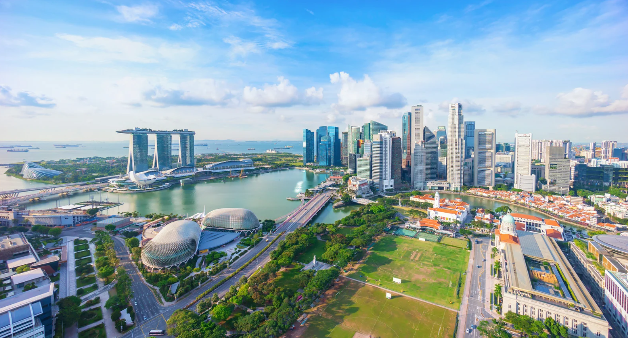 Aerial view of Singapore with Marina Bay Sands hotel, ArtScience Museum, and downtown skyline, featuring high-rise buildings, green spaces, and waterfront.