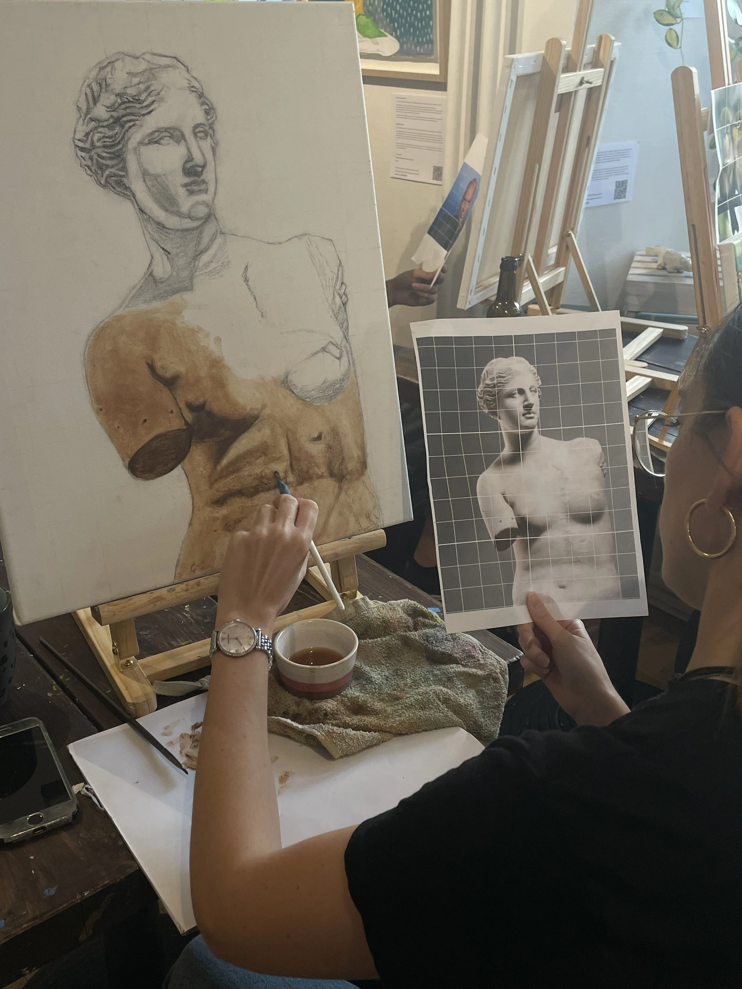 A person drawing a portrait of a woman with a grid on the photograph, at an art workshop or studio.