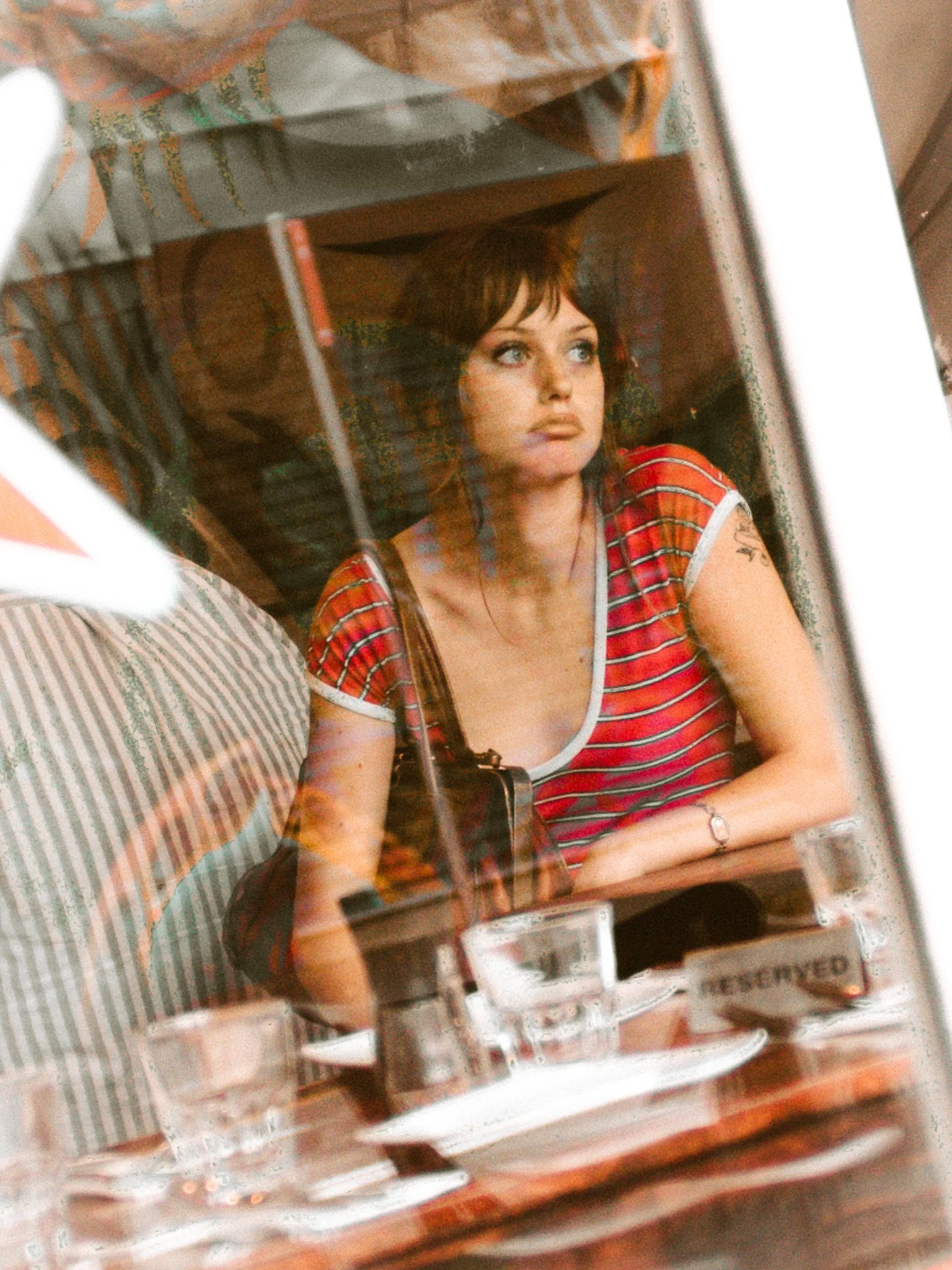 A young woman with short dark hair and blue eyes looking out the window. She is wearing a red and white striped shirt and a silver bracelet.