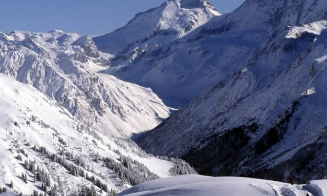 Snow-covered mountains with a valley and clear blue sky.
