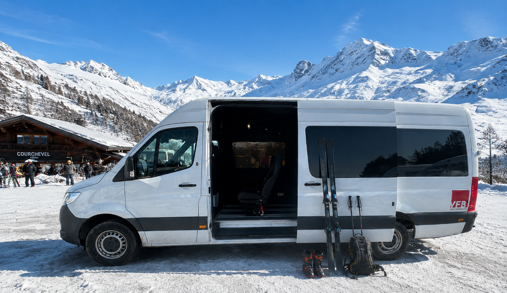 White van parked in snowy mountain landscape with skiing equipment including skis, ski boots, and backpacks in front of the van.